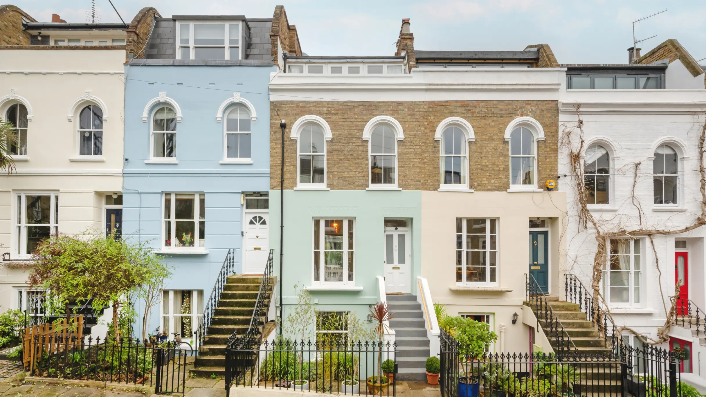 Row of blue, sage, and cream terraced houses with steps leading the front door and plant pots in front 