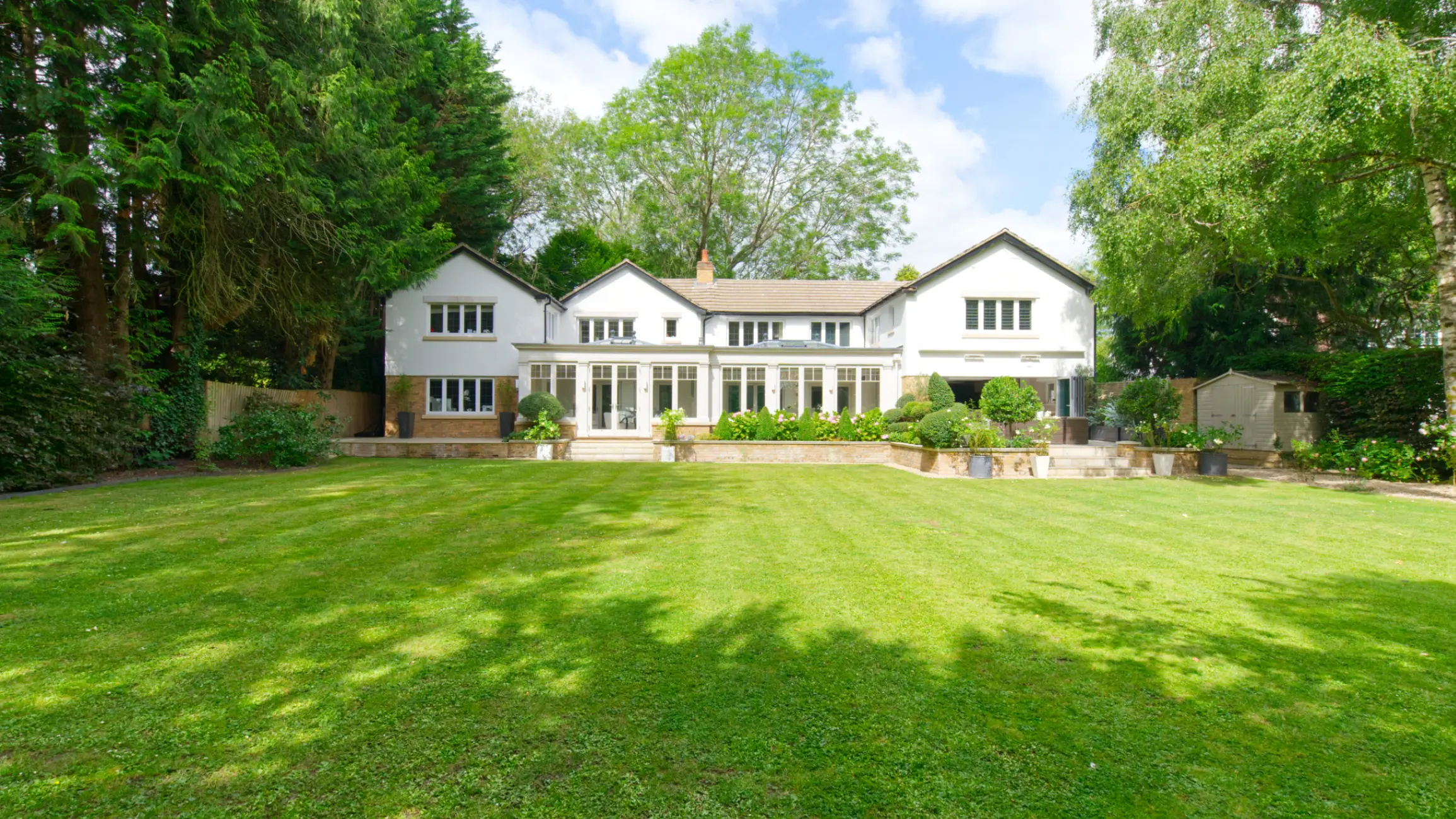 Exterior of a large country house with a big rear garden, surrounded by mature trees
