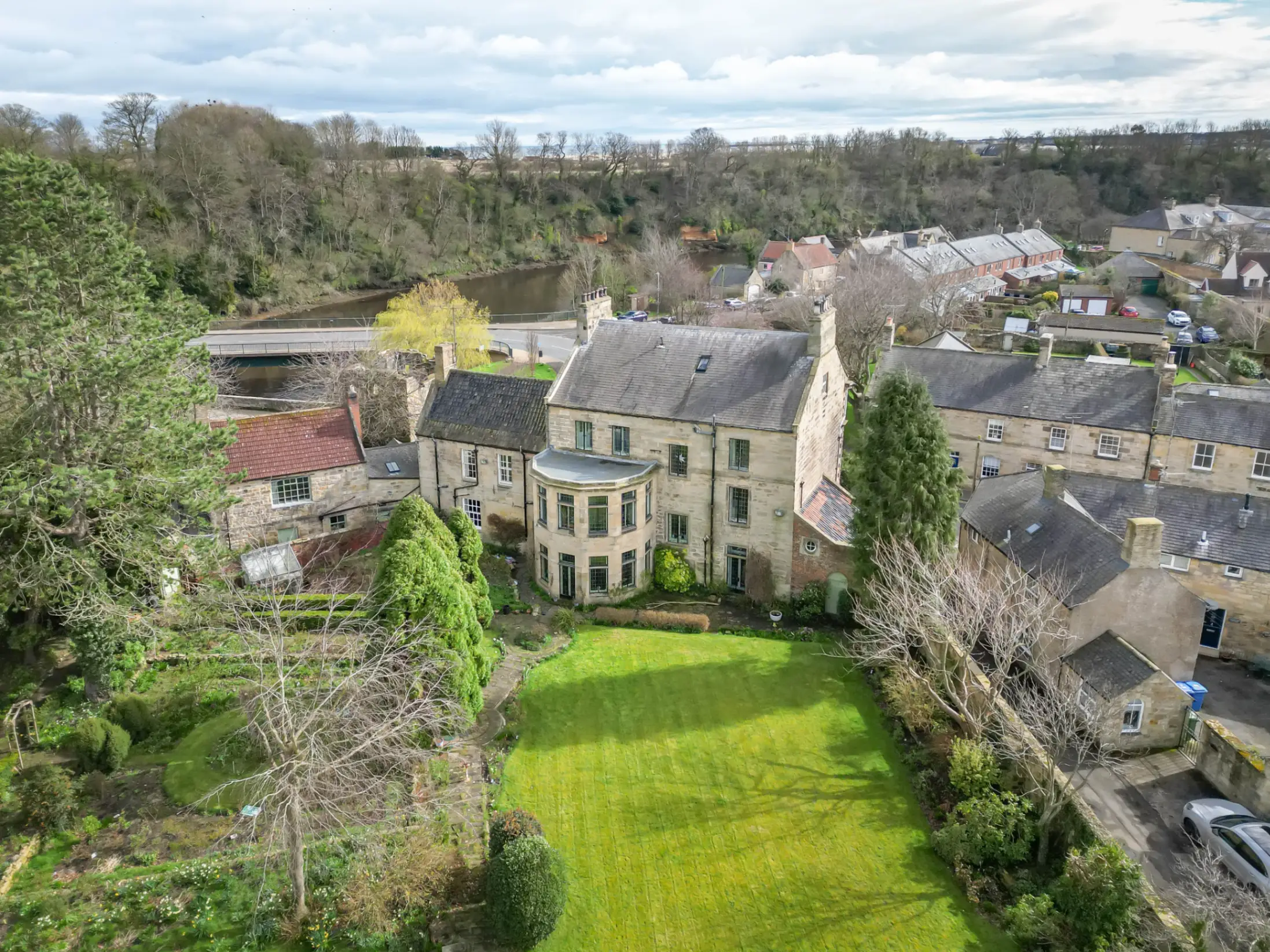 Exterior of a period country home surrounded by trees and other period homes, with a back garden in the foreground