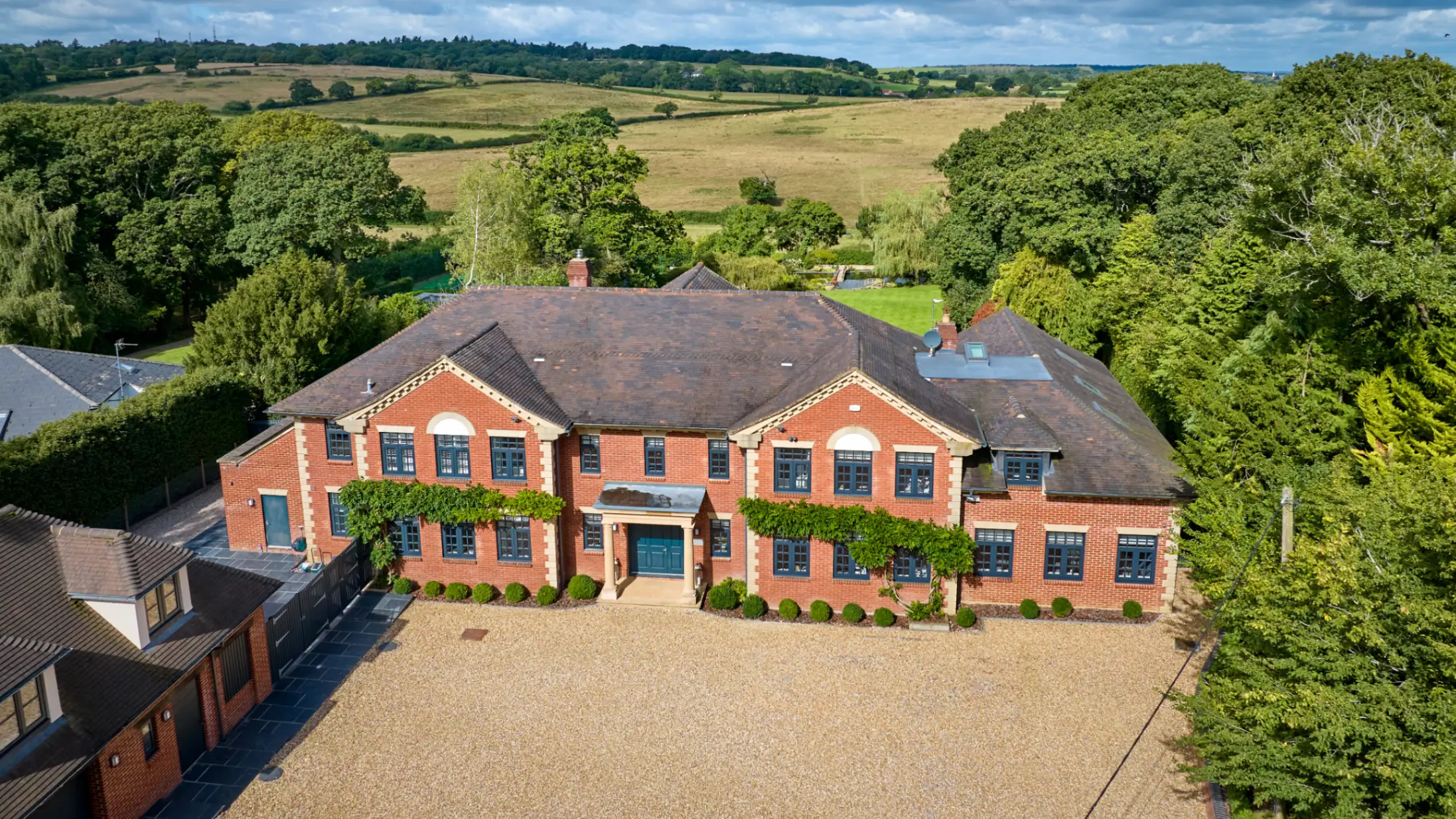 Large red brick country house with rolling fields and nature trees in the background