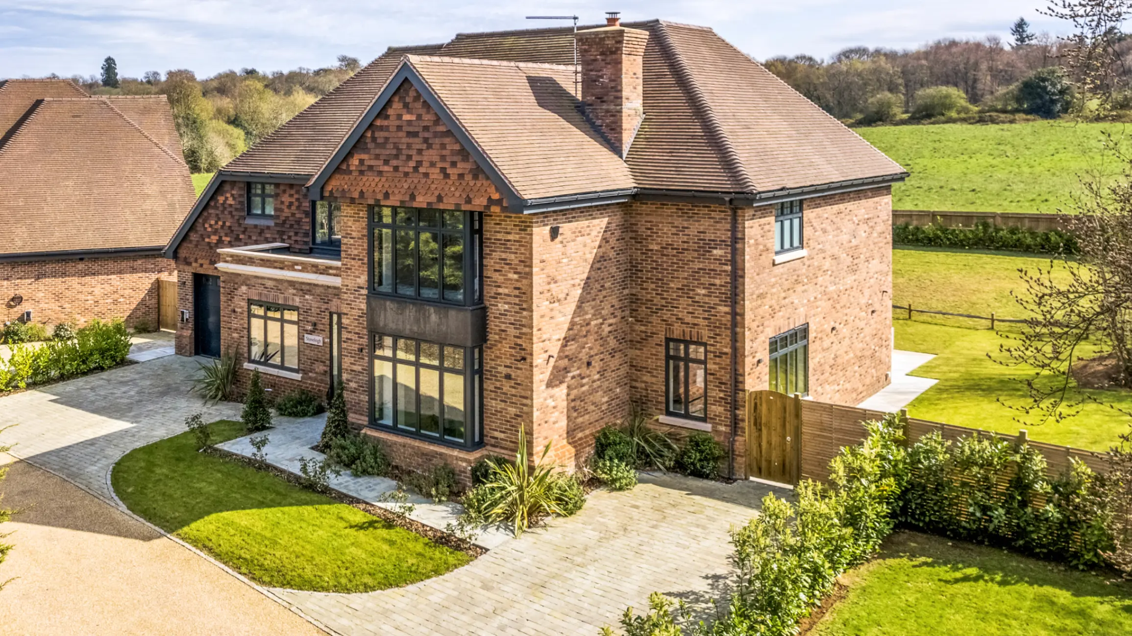 Exterior of a detached brick house with a front garden and large fields in the background with mature trees 