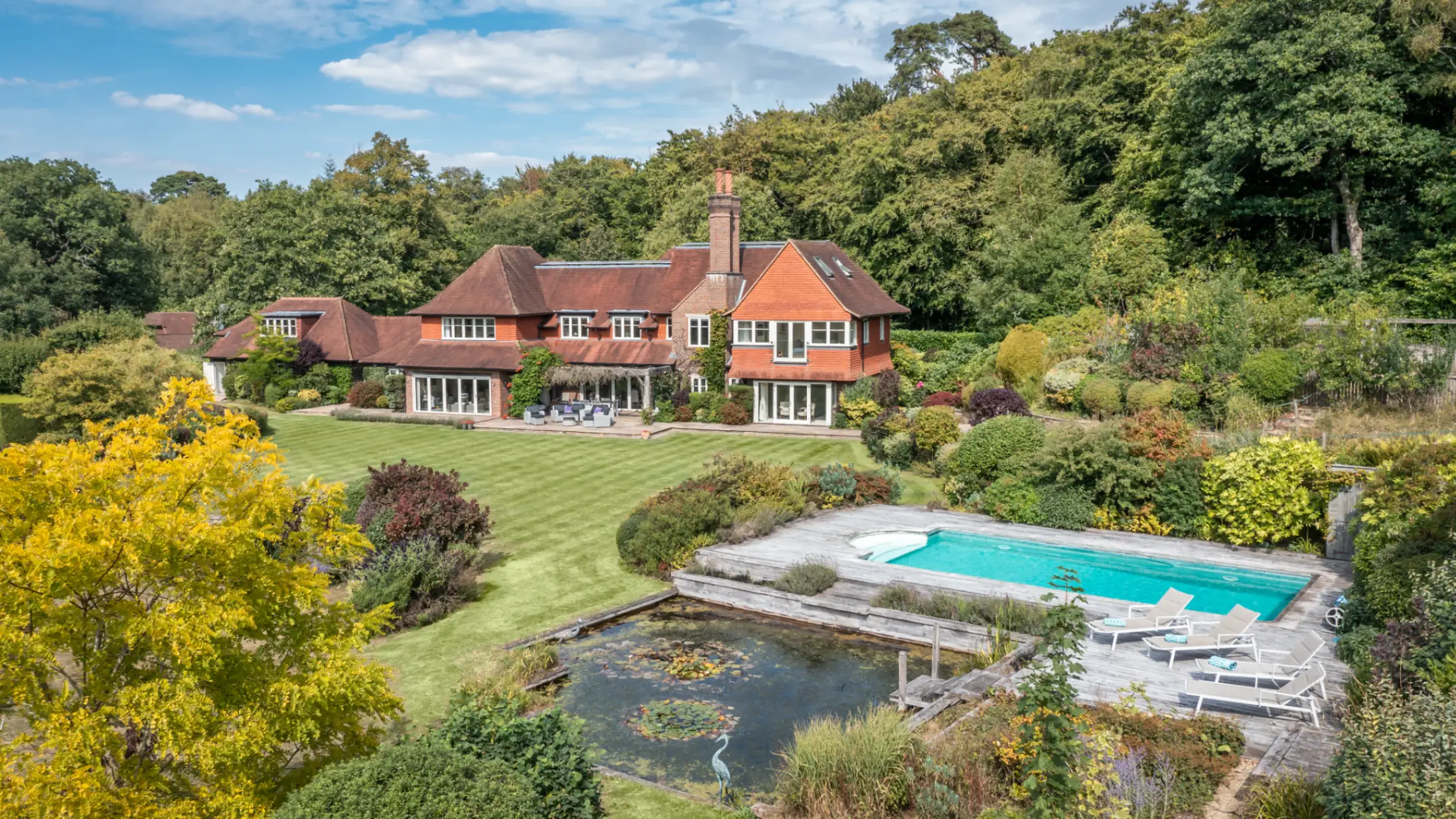 exterior-of-red-brick-country-house-in-surrey-surrounded-by-large-mature-trees-with-a-large-front-garden-including-a-swimming-pool
