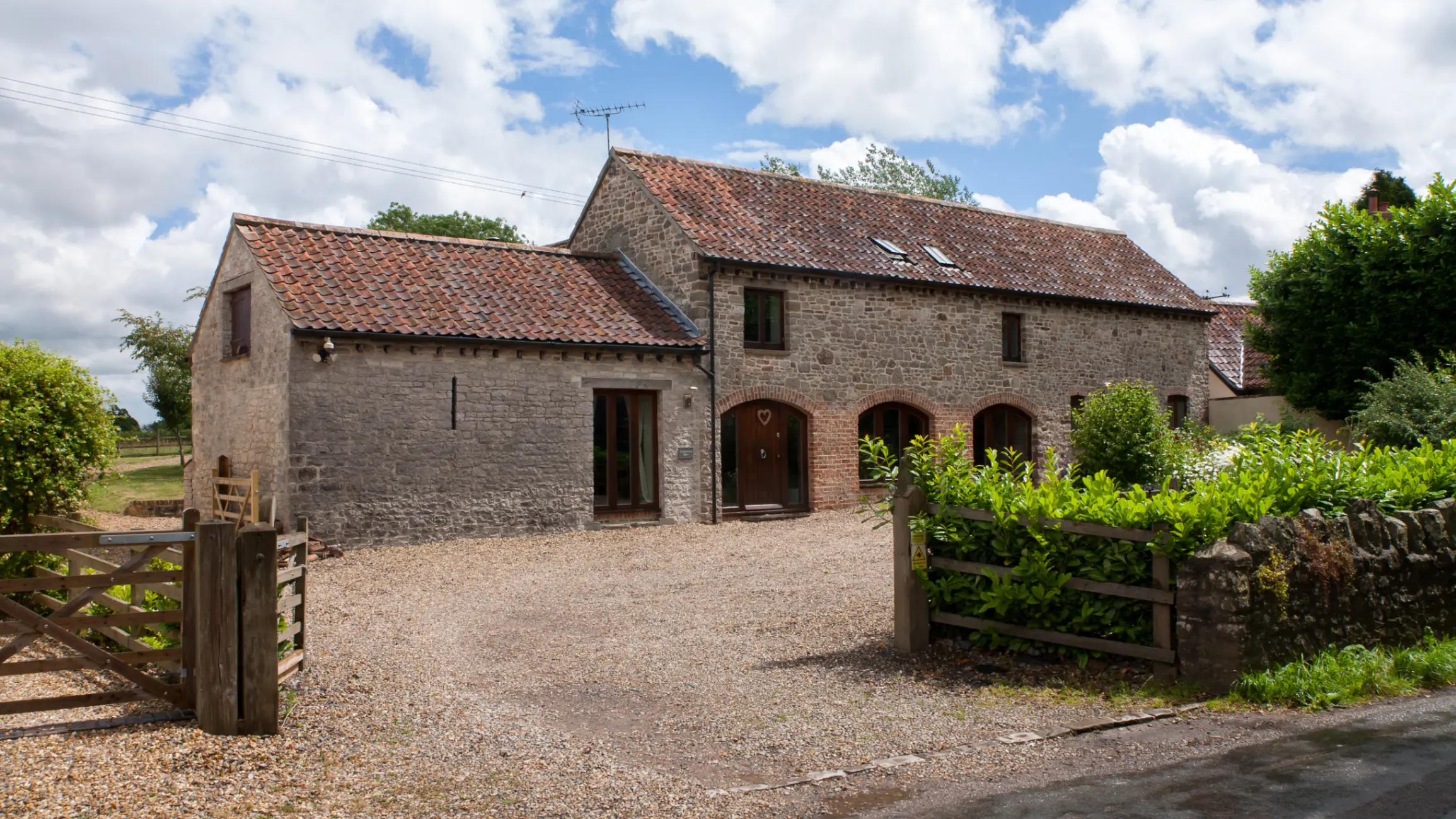 Exterior of a brown barn conversion with a gravel drive and green bushes in the front garden