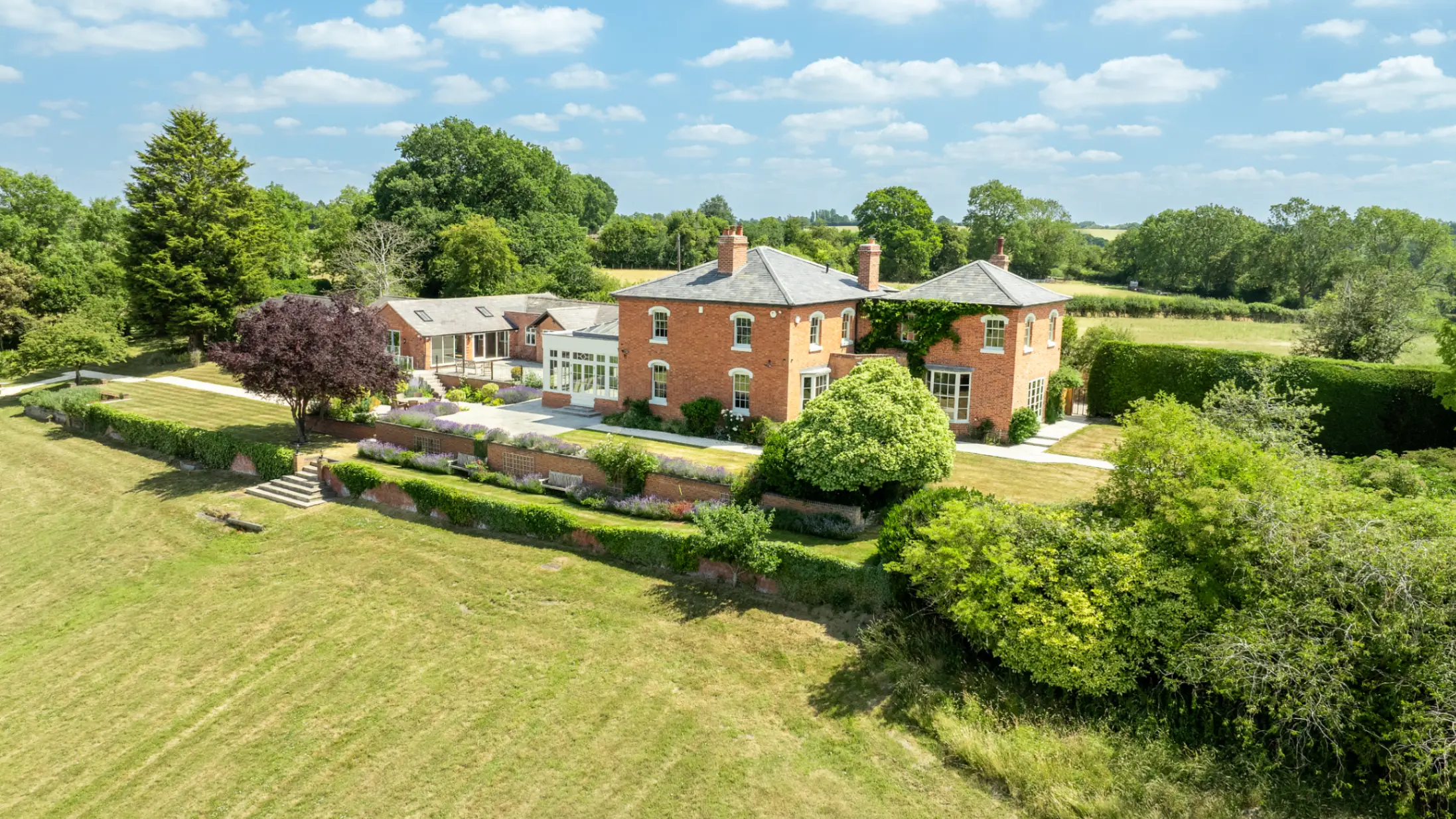 Exterior of a large country house with extensive green grounds and mature trees