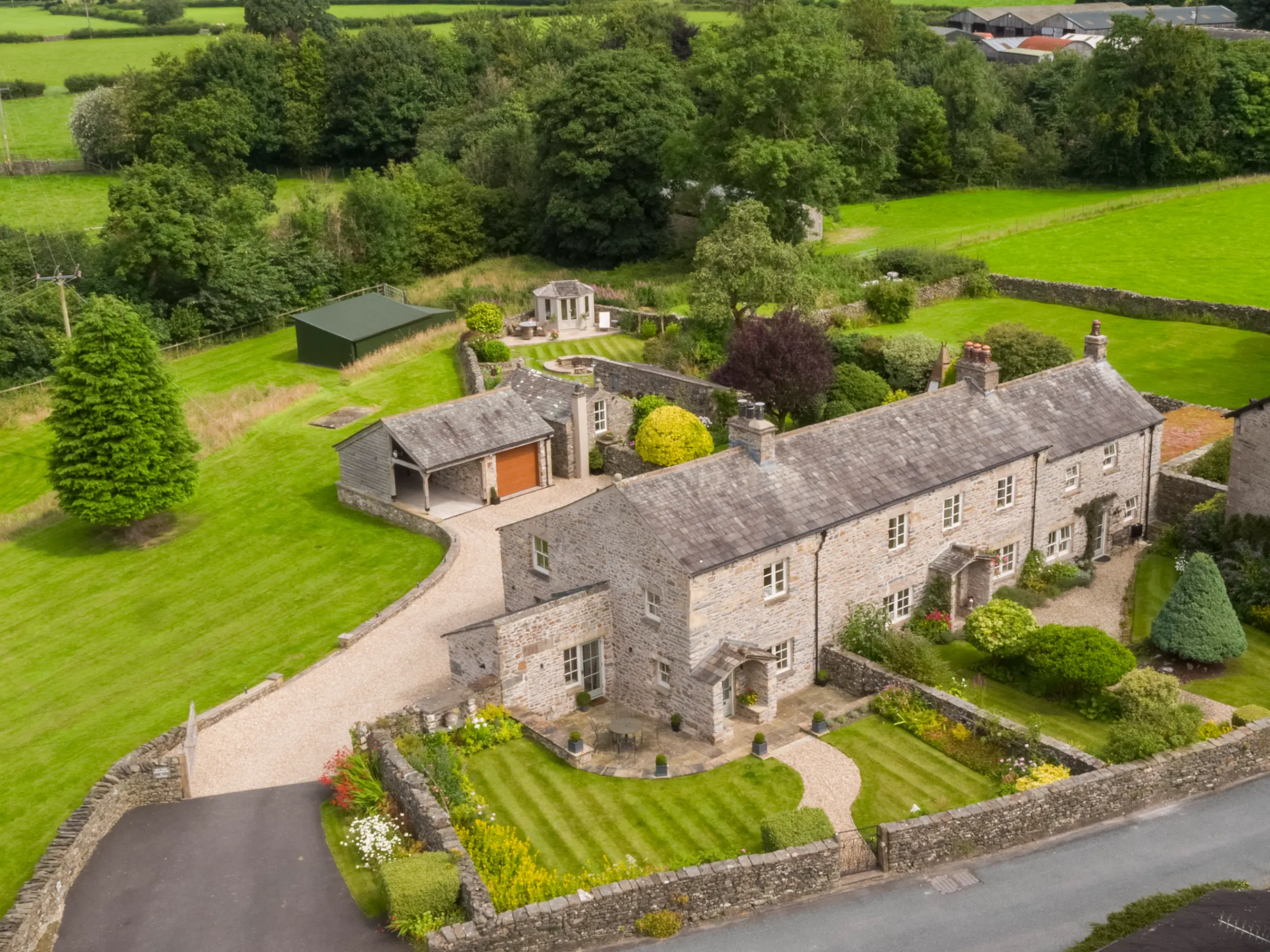 Exterior of a large farmhouse, surrounded by green fields and mature trees