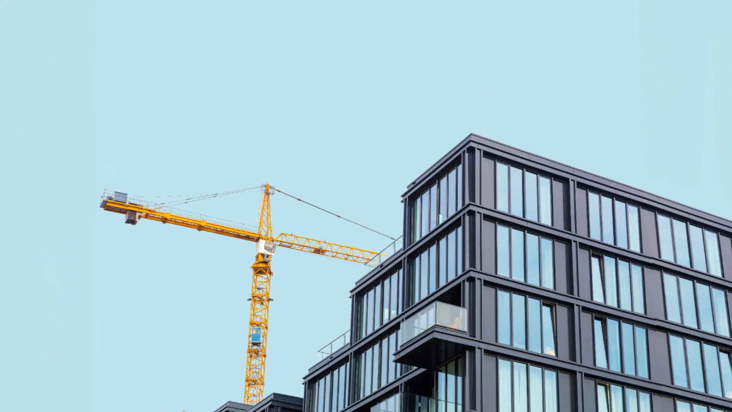 Modern apartment building under construction with a crane in the foreground against a clear blue sky.
