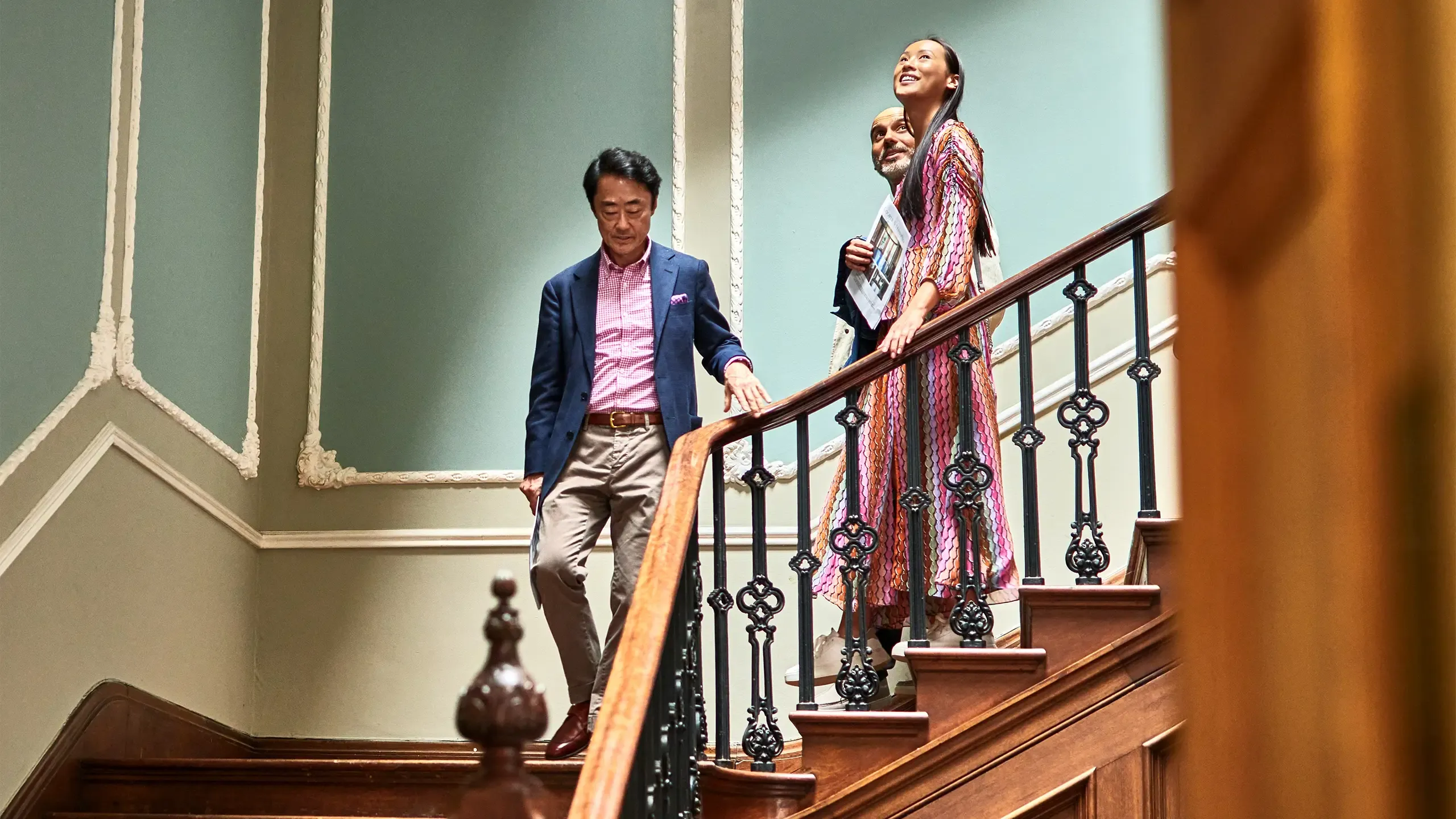 Wealthy couple walking down staircase with Japanese real estate agent during viewing in spacious potential new home, opportunity, potential, home ownership