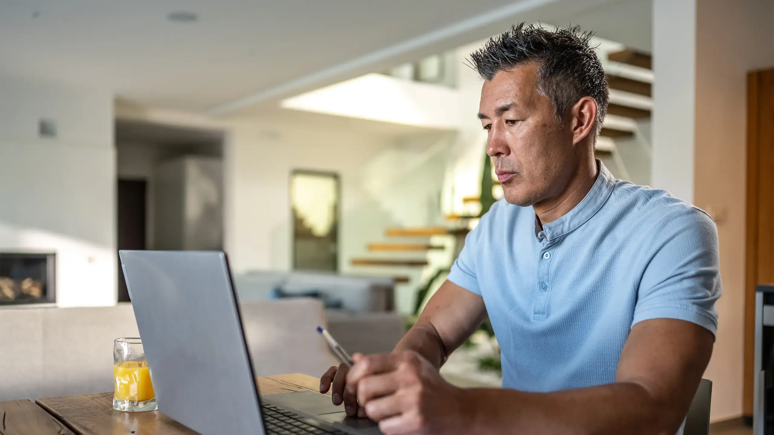 Mature man working on laptop with diary while sitting on chair at home.