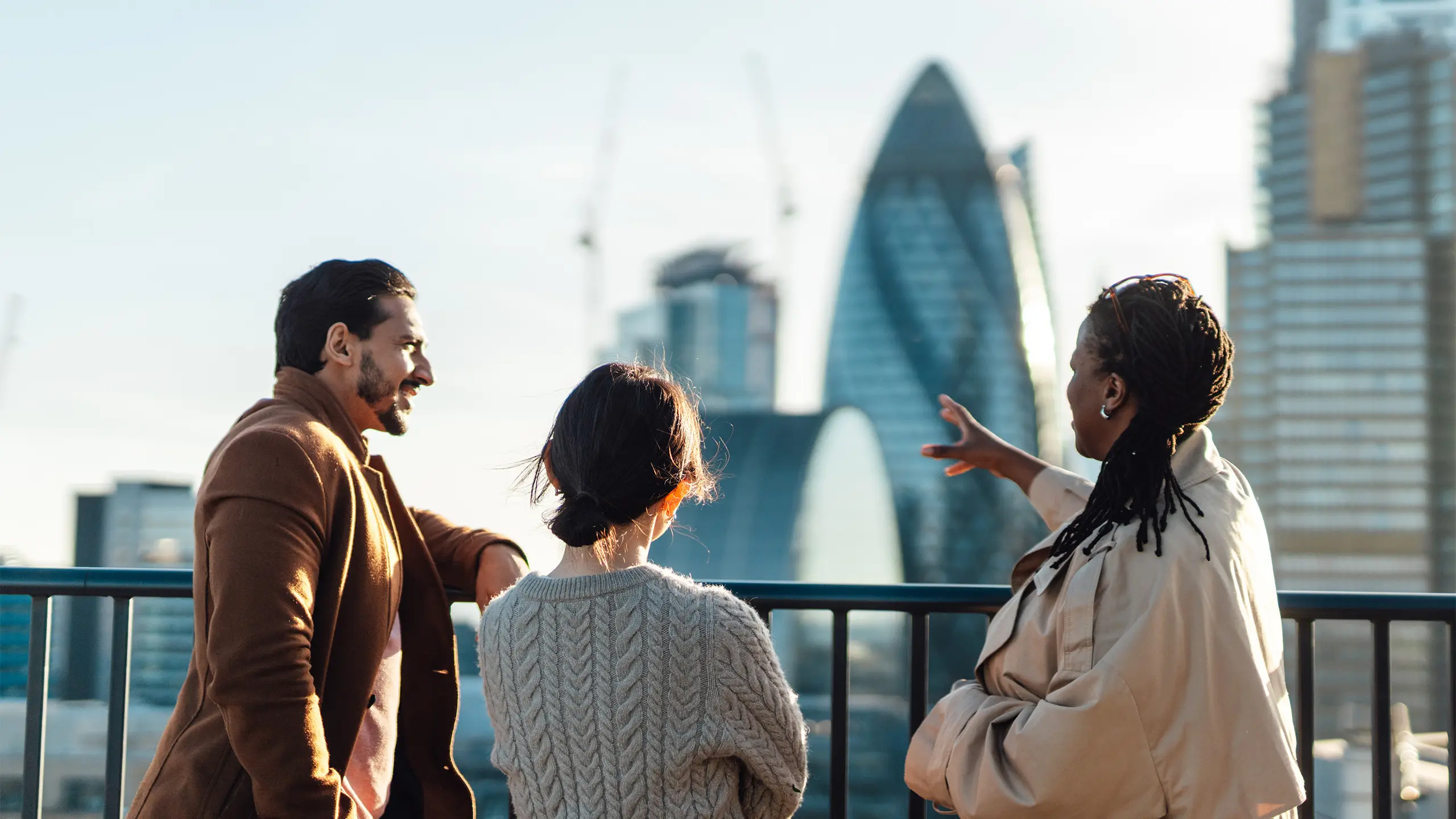 Multiracial business coworkers looking out across city at sunrise. Rear view of business people standing on rooftop in an office building against cityscape of London. Startup founders and partners looking to the bright future.