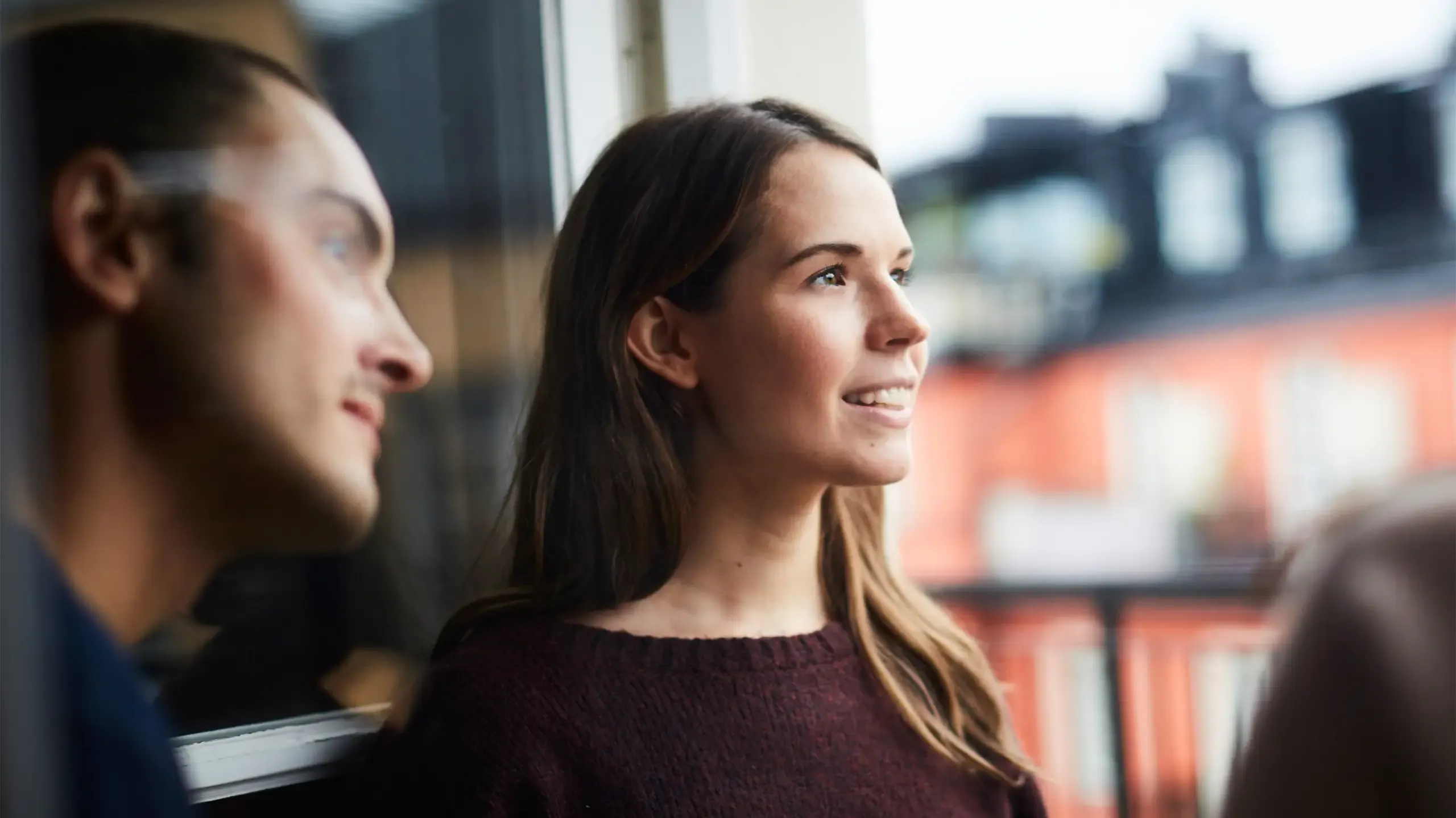 Smiling woman with friends looking away while standing in balcony of rental apartment