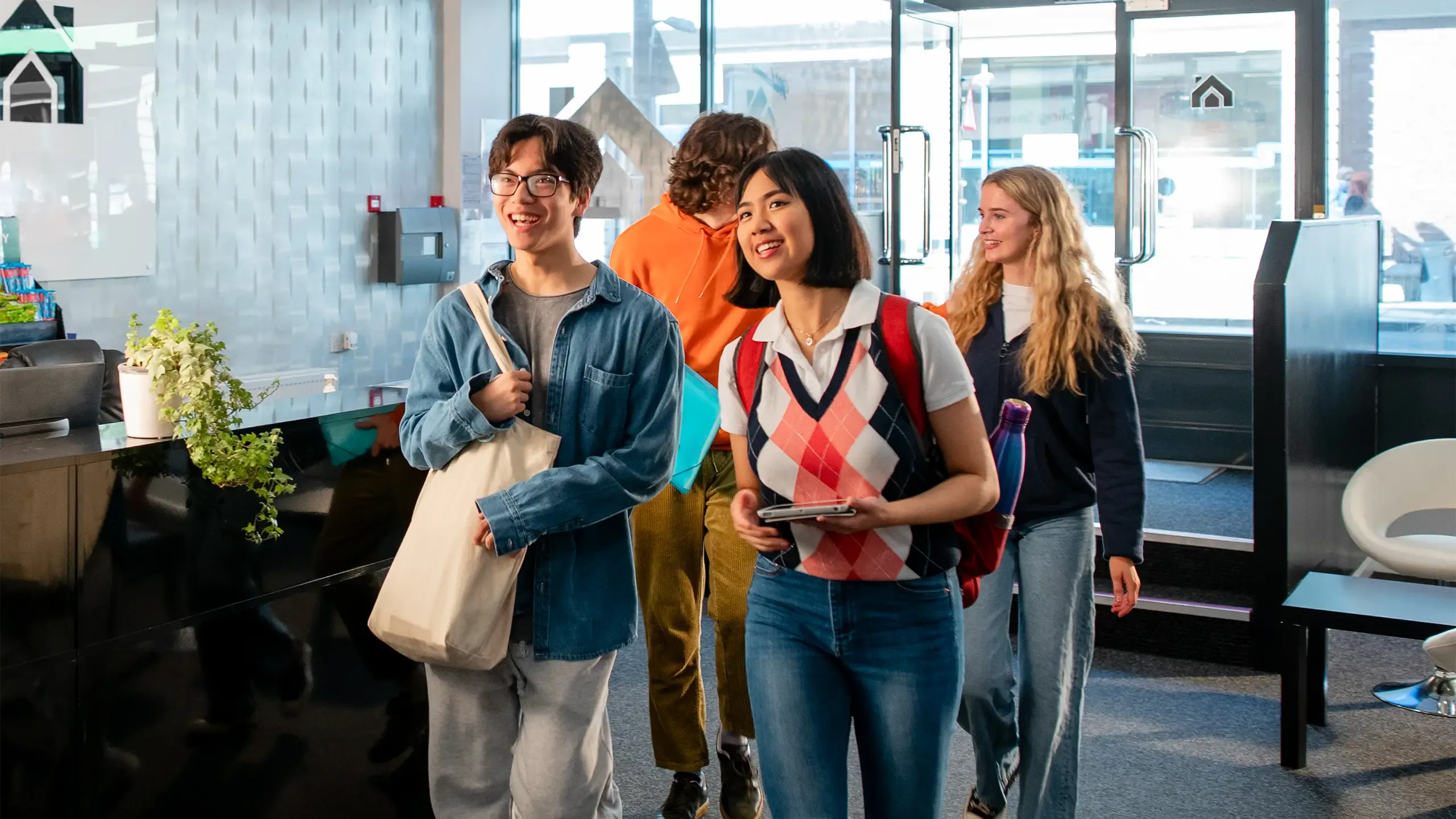 Wide angle view of four new University students walking into their student accommodation in Sunderland in the north-east of England what are they was carrying a reusable toilet bag and they are walking through the reception area of the building.