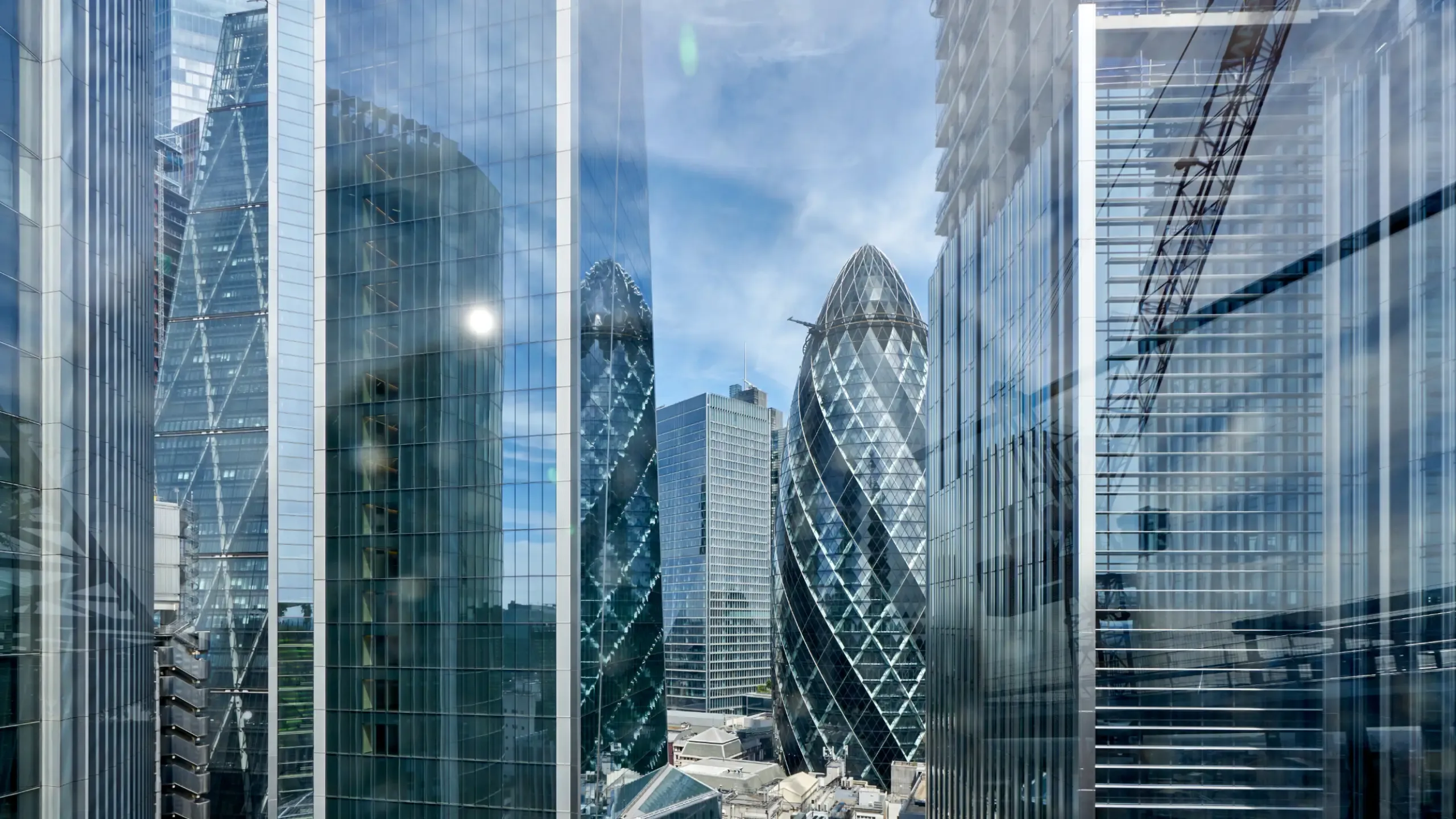 The Gherkin, formally 30 St Mary Axe and previously known as the Swiss Re Building, is a commercial skyscraper in London's primary financial district, the City of London. Here viewed looking north through glass officer buildings from the roof top of a nearby office building.