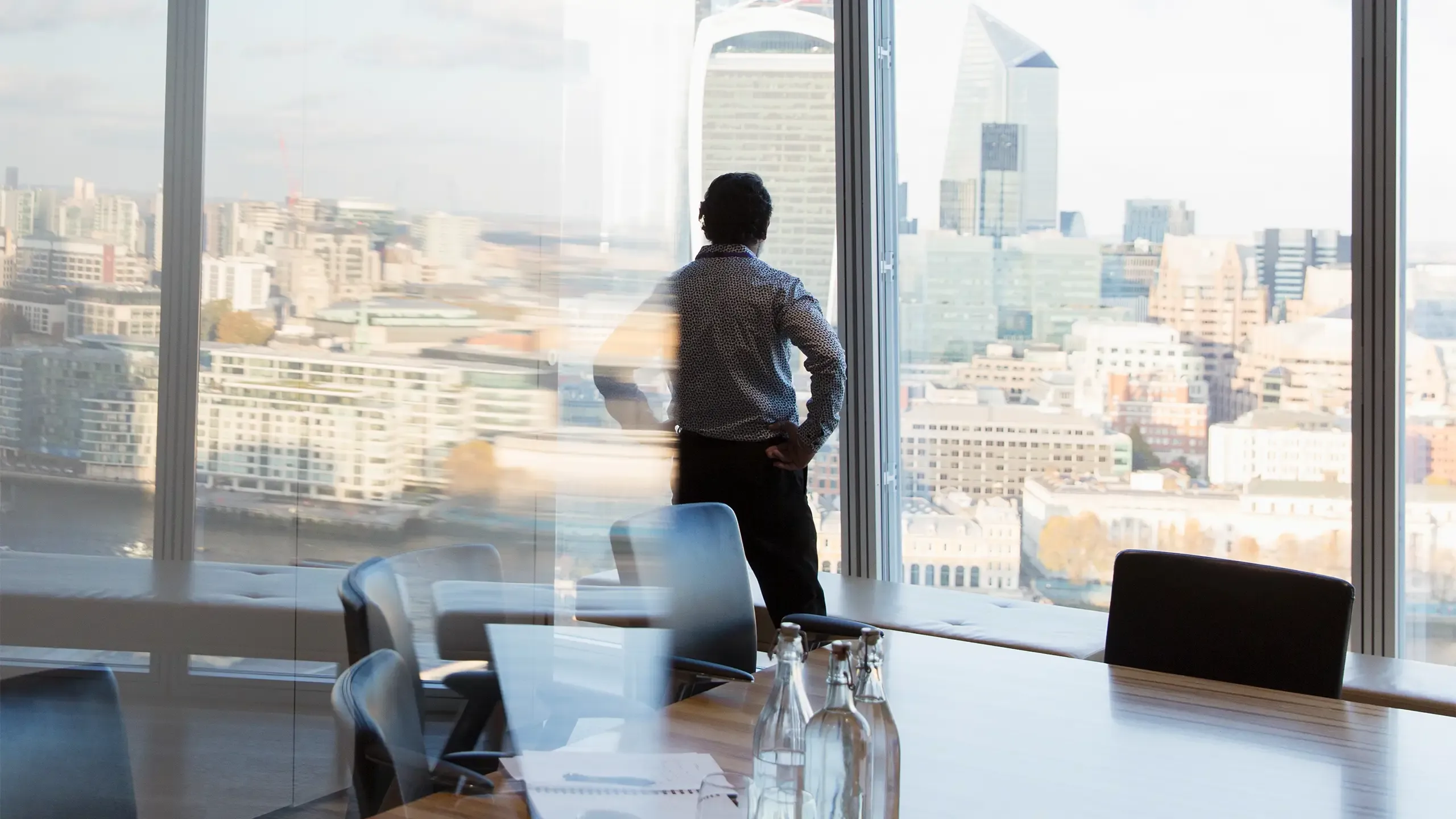 Thoughtful corporate businessman looking out highrise office window at city view, London, UK, multiple exposure