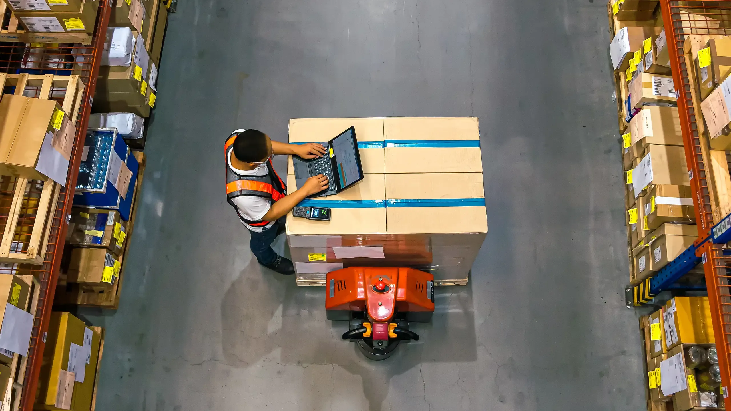 Top view of warehouse worker using laptop to check location of goods.