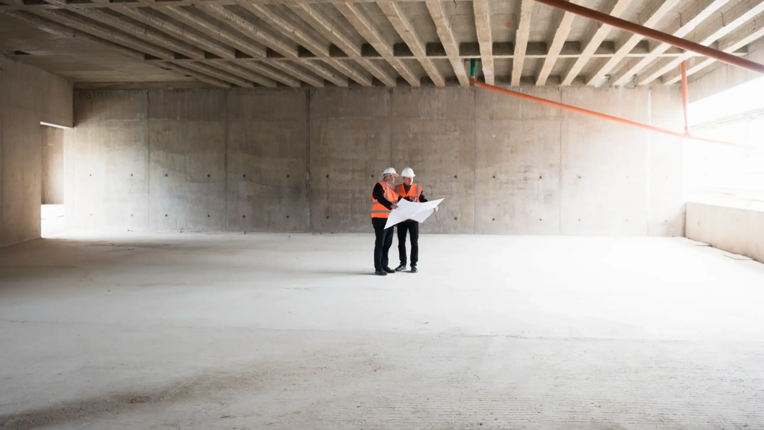 Two men with plan wearing safety vests talking in building under construction