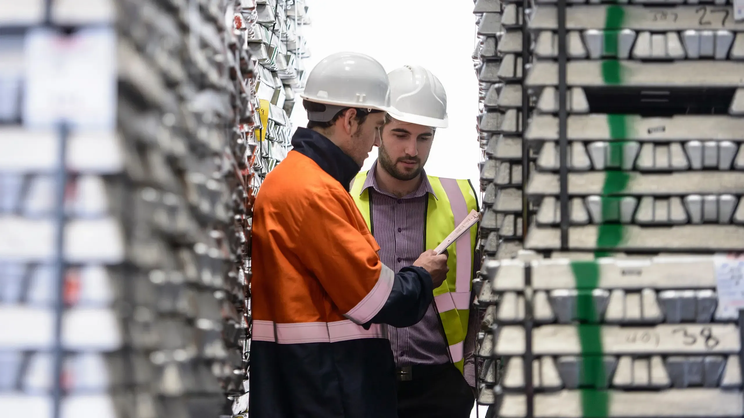 Workers inspecting stacks of aluminium ingots in warehouse