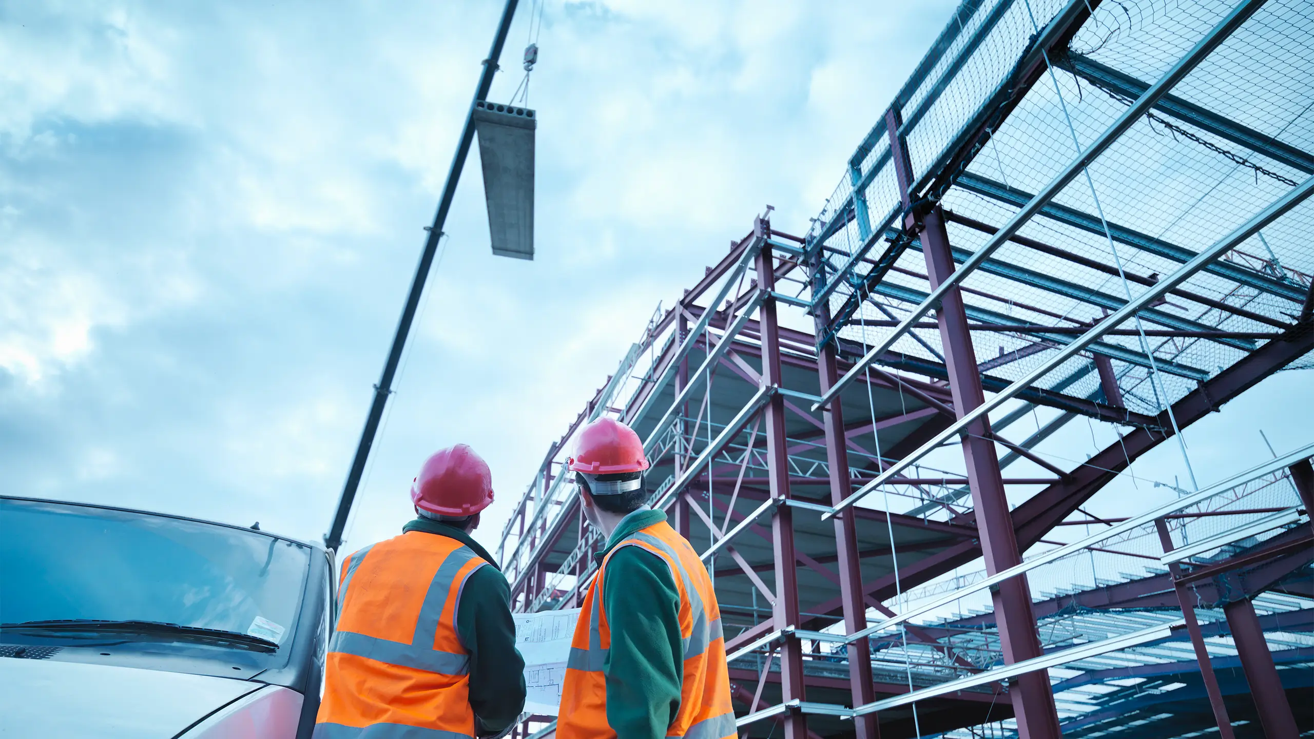 Workmen watching crane lifting roof panels onto steel construction frame on building site