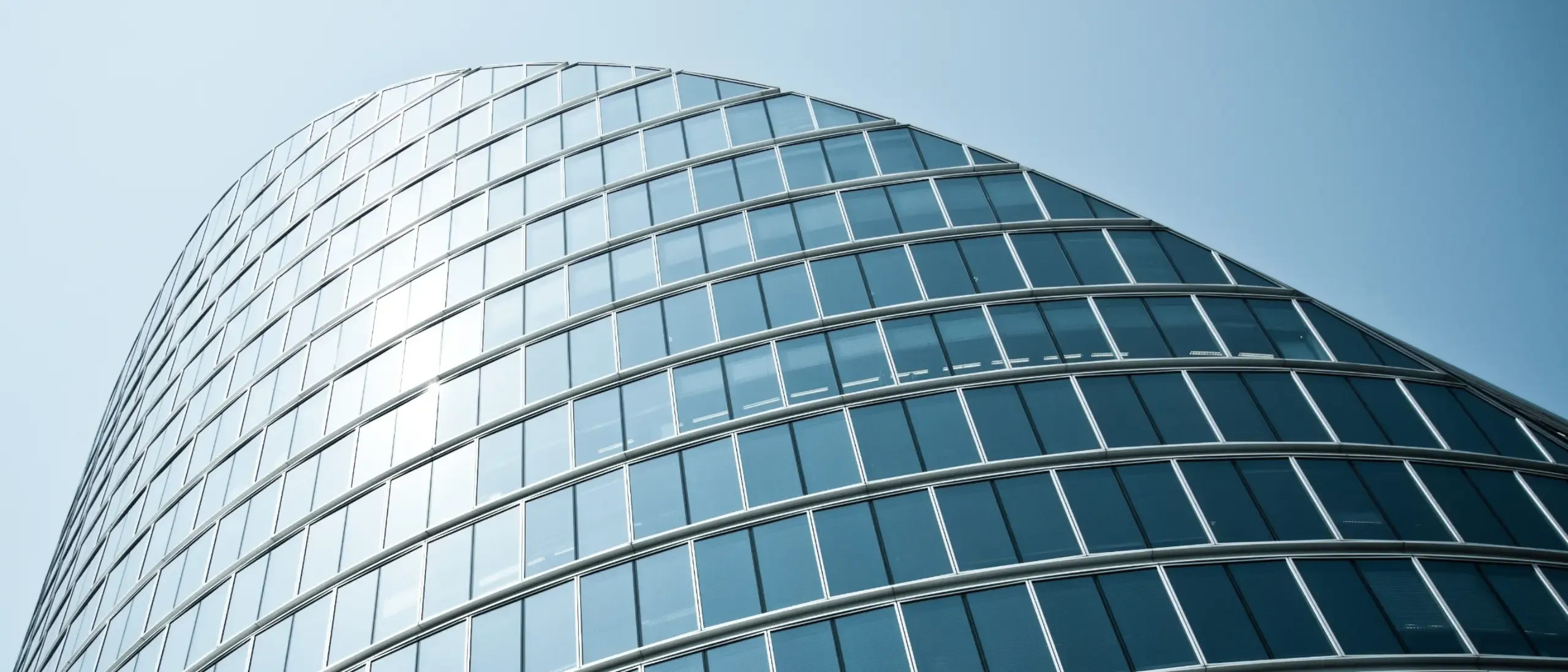 A curved, modern office building against a blue sunny sky