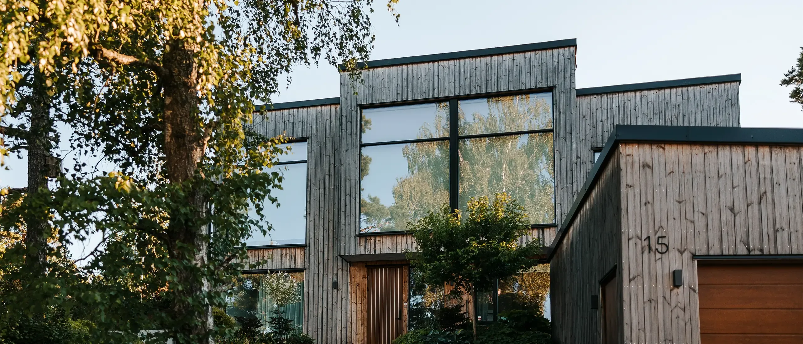 Modern wooden house with driveway and trees against sky