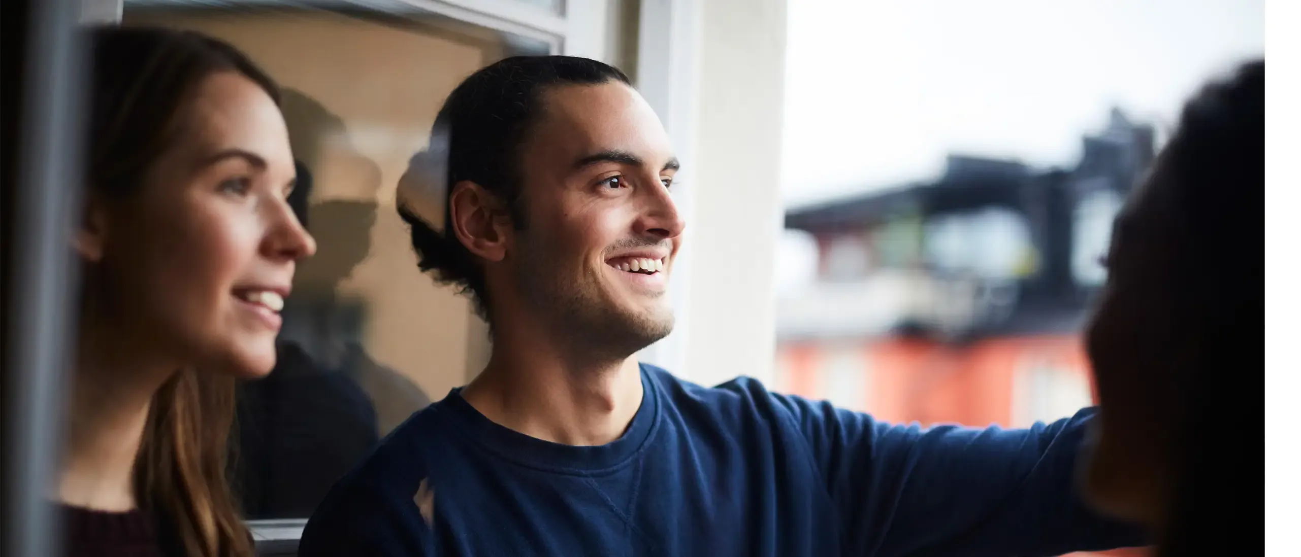 Smiling man with friends looking through window while standing in rental apartment