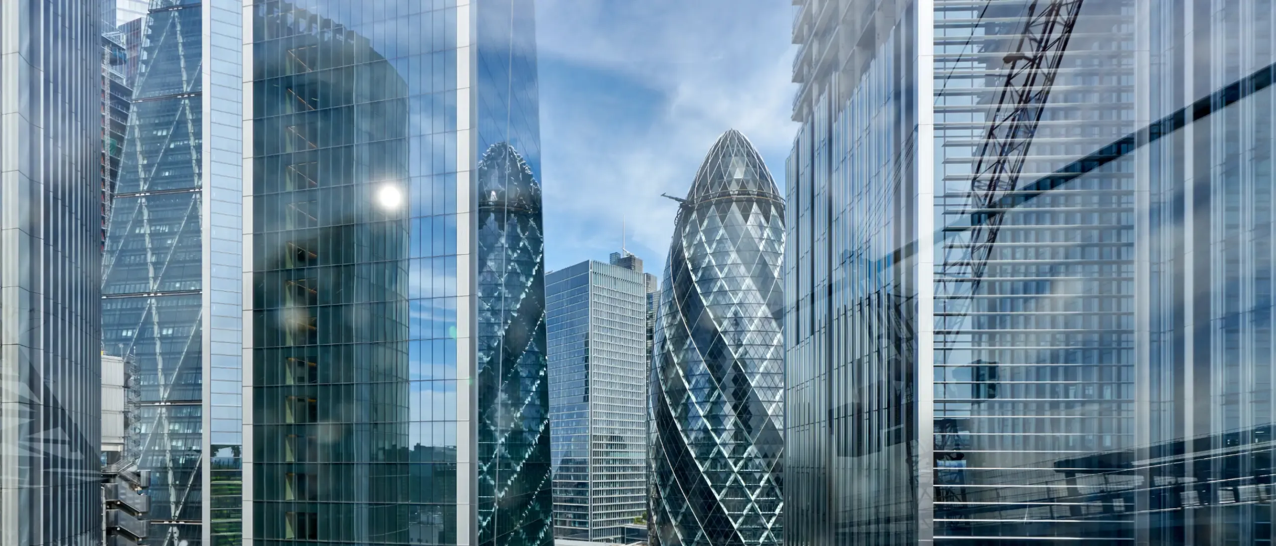 The Gherkin, formally 30 St Mary Axe and previously known as the Swiss Re Building, is a commercial skyscraper in London's primary financial district, the City of London. Here viewed looking north through glass officer buildings from the roof top of a nearby office building.