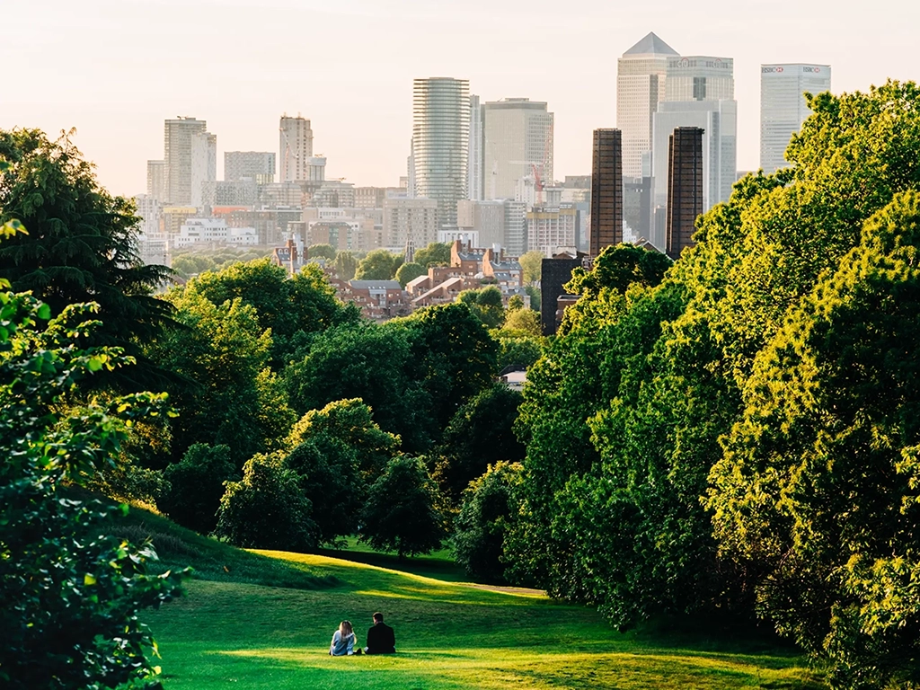 A couple sit in Greenwich Park, London looking at the Canary Wharf skyline