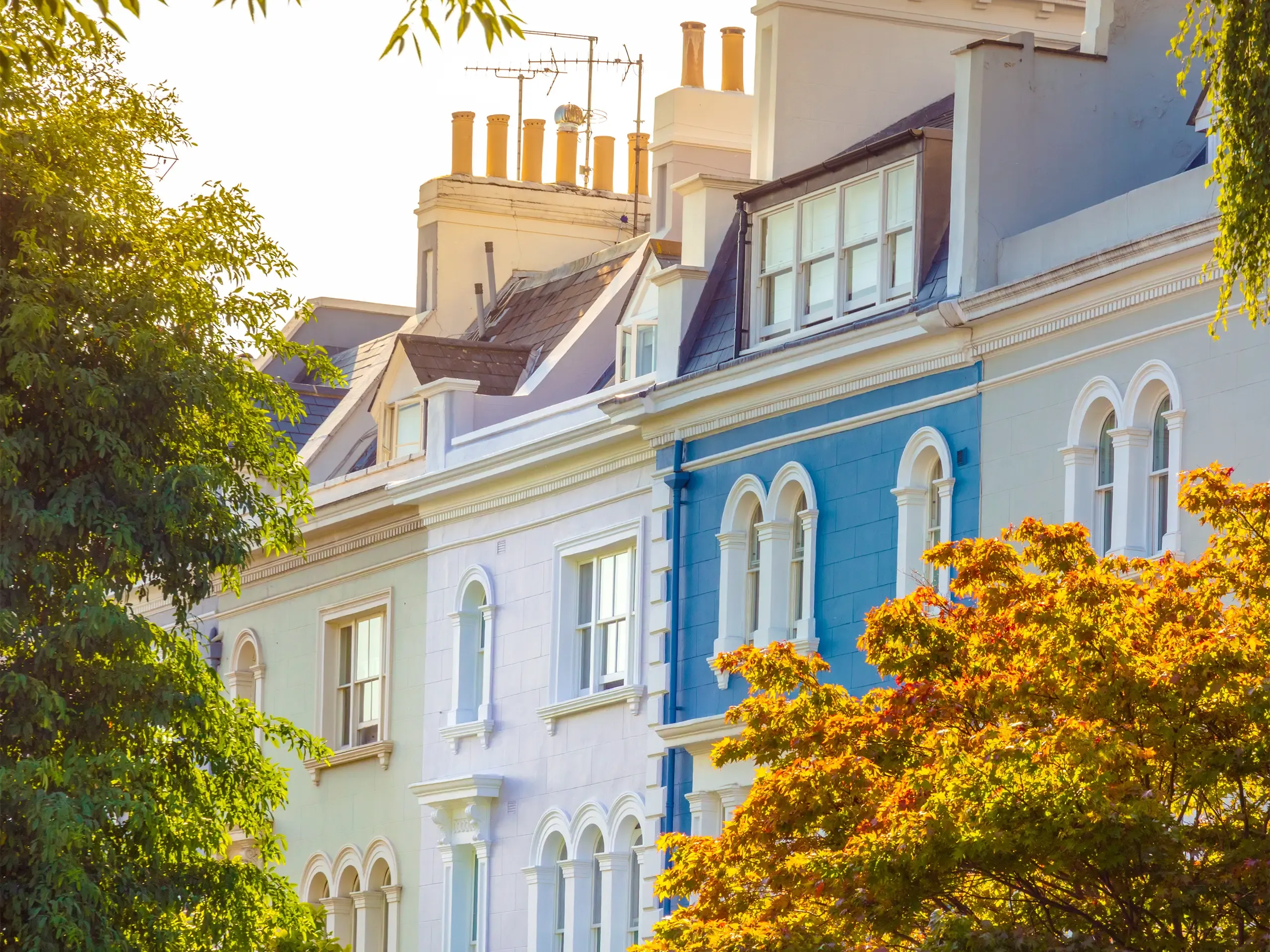UK, London, Notting Hill. The facade of a luxurious traditional Regency style townhouses painted in bright colors and seen through Autumn trees