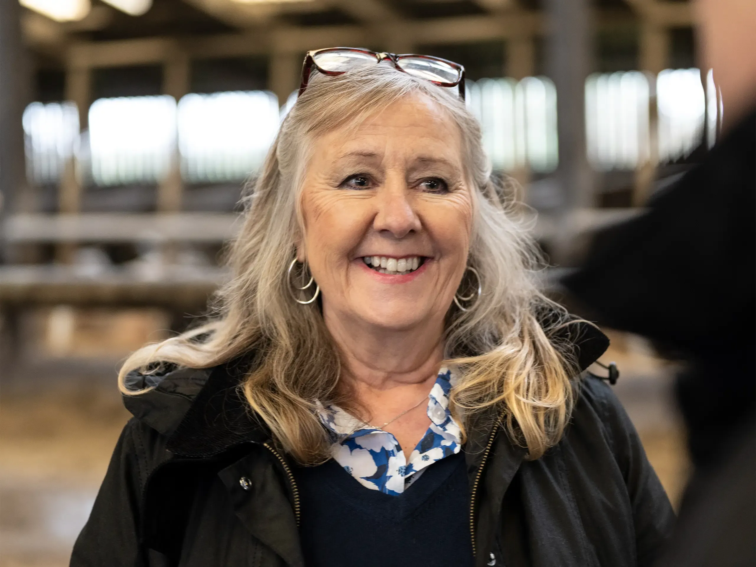 Over the shoulder waist-up view of cheerful mid 60s businesswoman standing and conversing with farmer in barn.