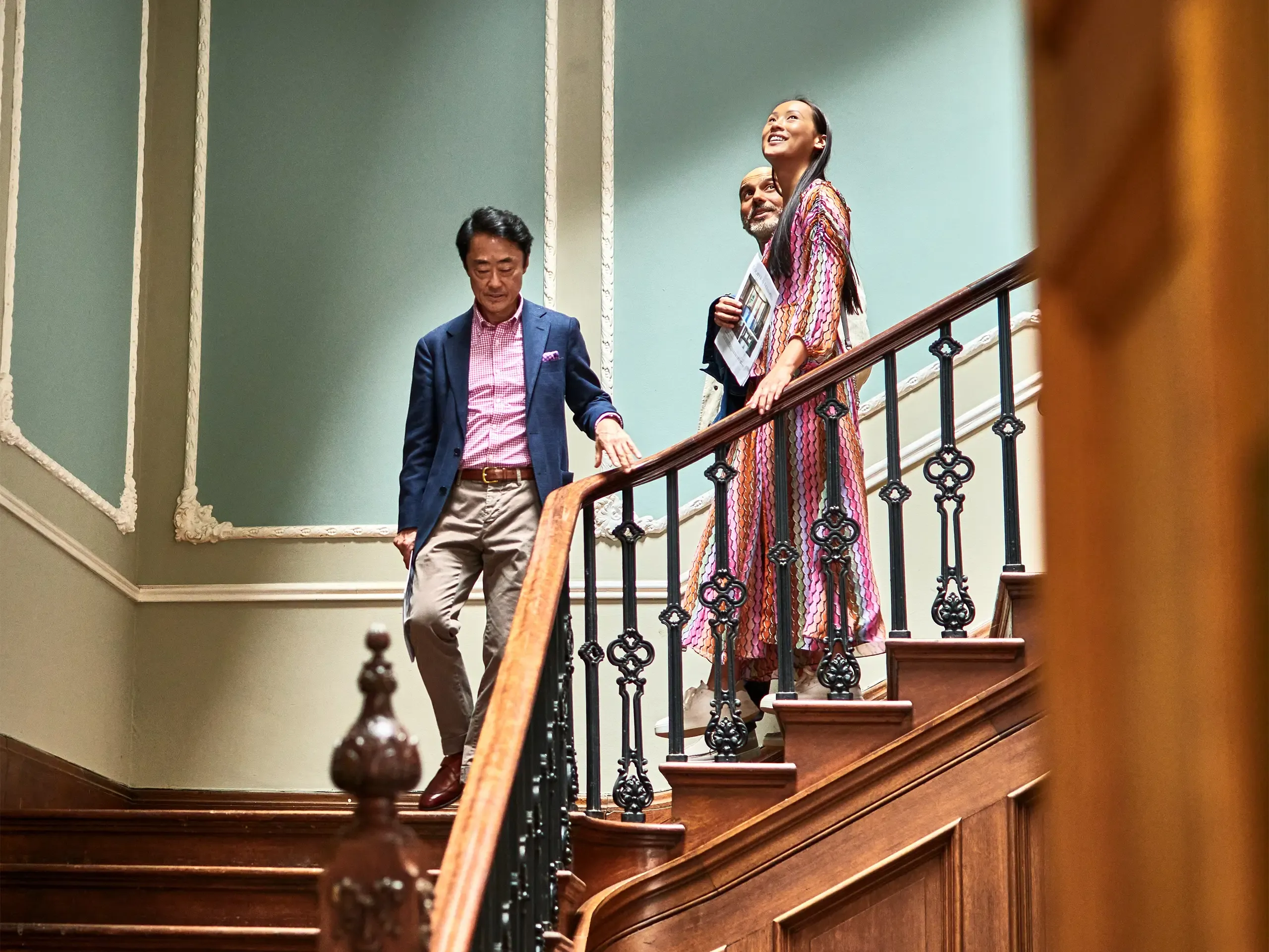 Wealthy couple walking down staircase with Japanese real estate agent during viewing in spacious potential new home, opportunity, potential, home ownership