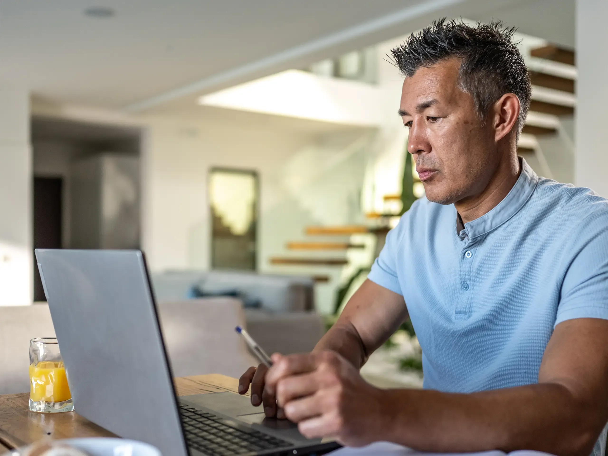Mature man working on laptop with diary while sitting on chair at home.