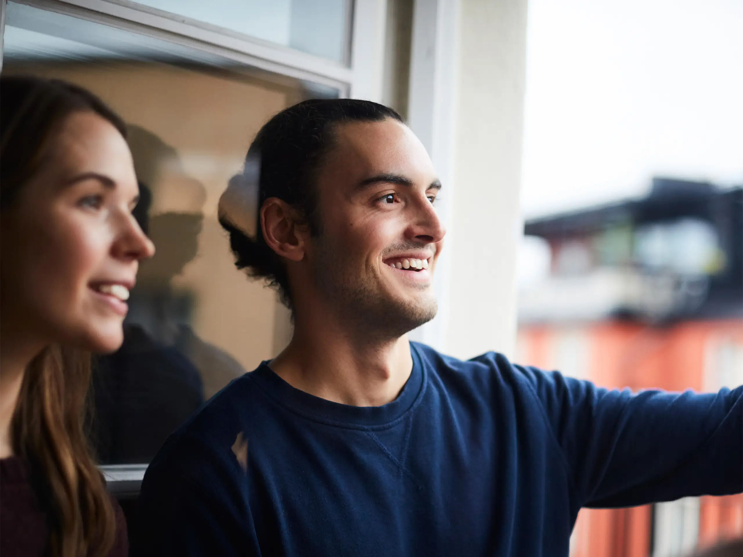Smiling man with friends looking through window while standing in rental apartment