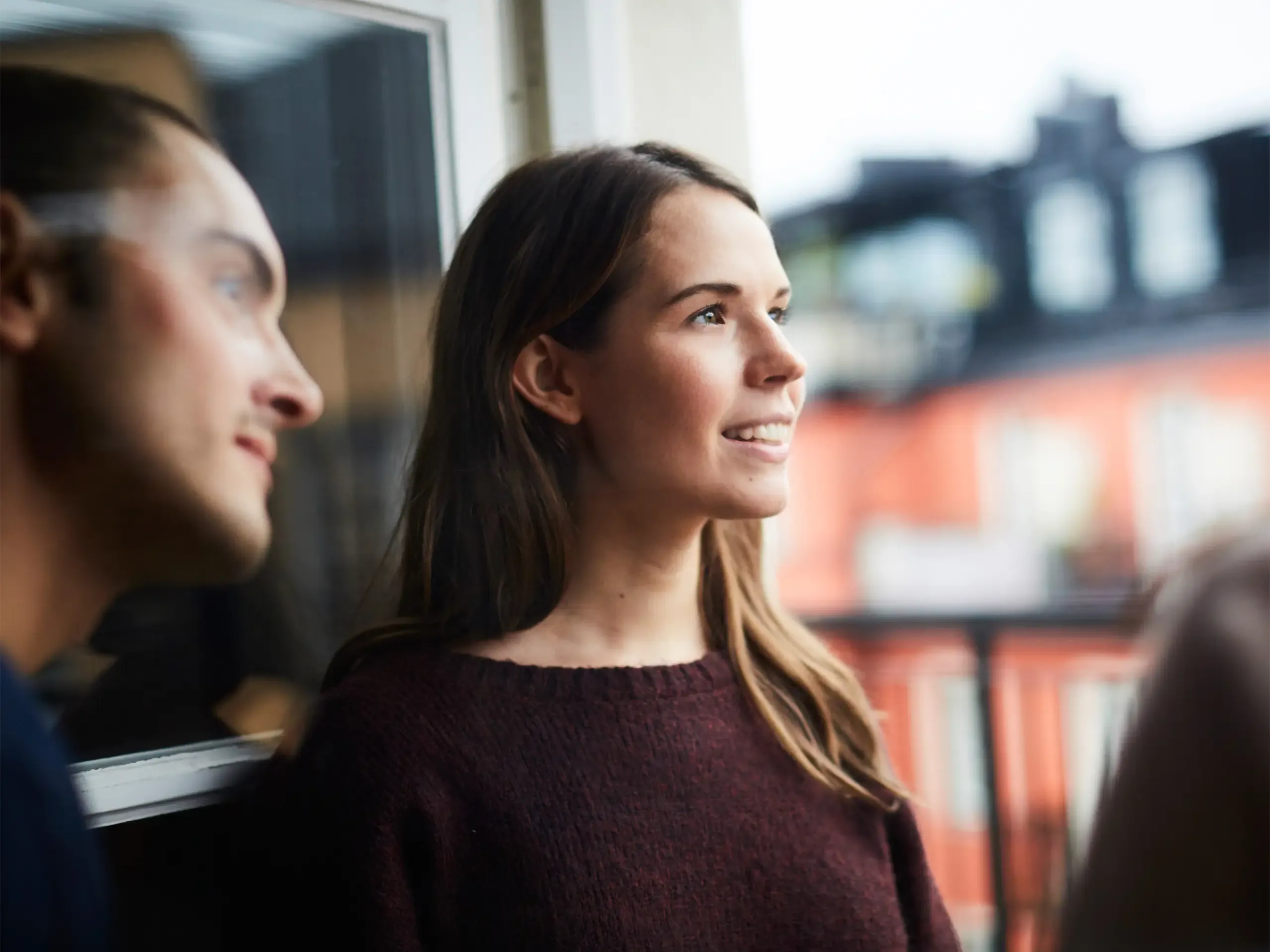 Smiling woman with friends looking away while standing in balcony of rental apartment