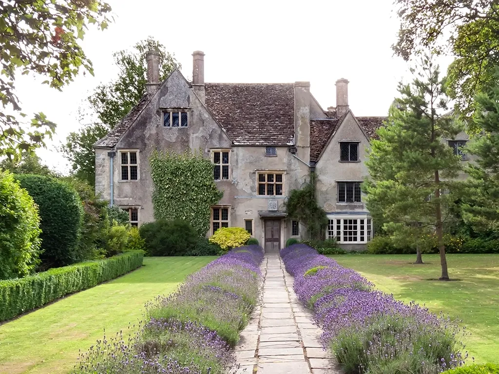 An old stately house with mature grounds on a summers day in the English countryside.