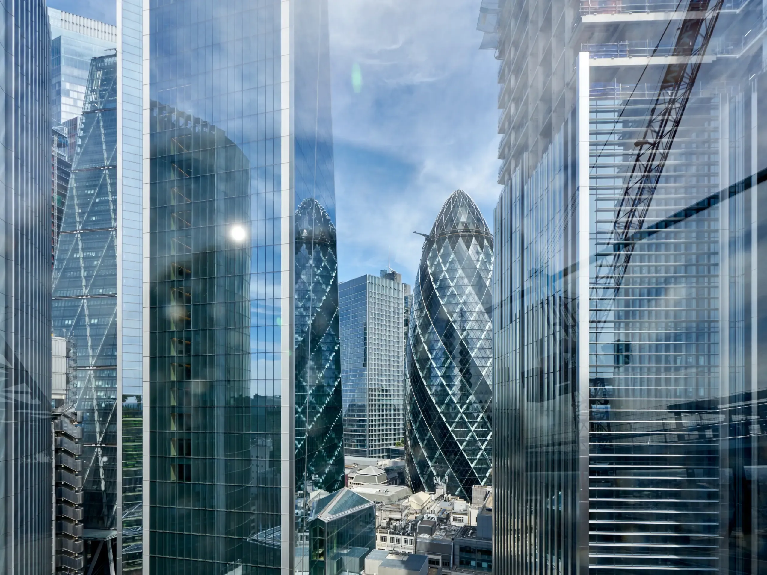 The Gherkin, formally 30 St Mary Axe and previously known as the Swiss Re Building, is a commercial skyscraper in London's primary financial district, the City of London. Here viewed looking north through glass officer buildings from the roof top of a nearby office building.