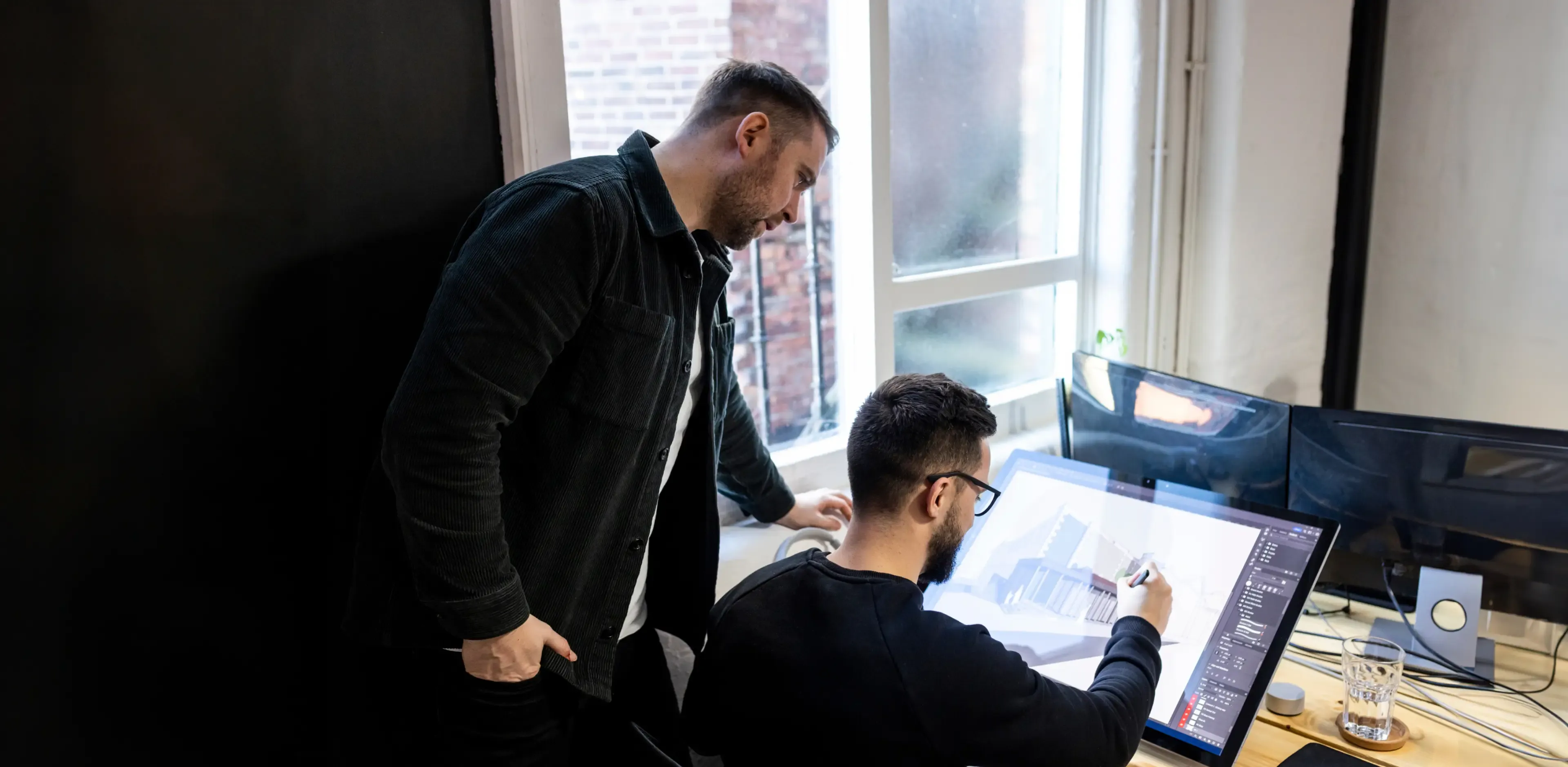 An architect works on a graphics tablet and has a discussion with a colleague