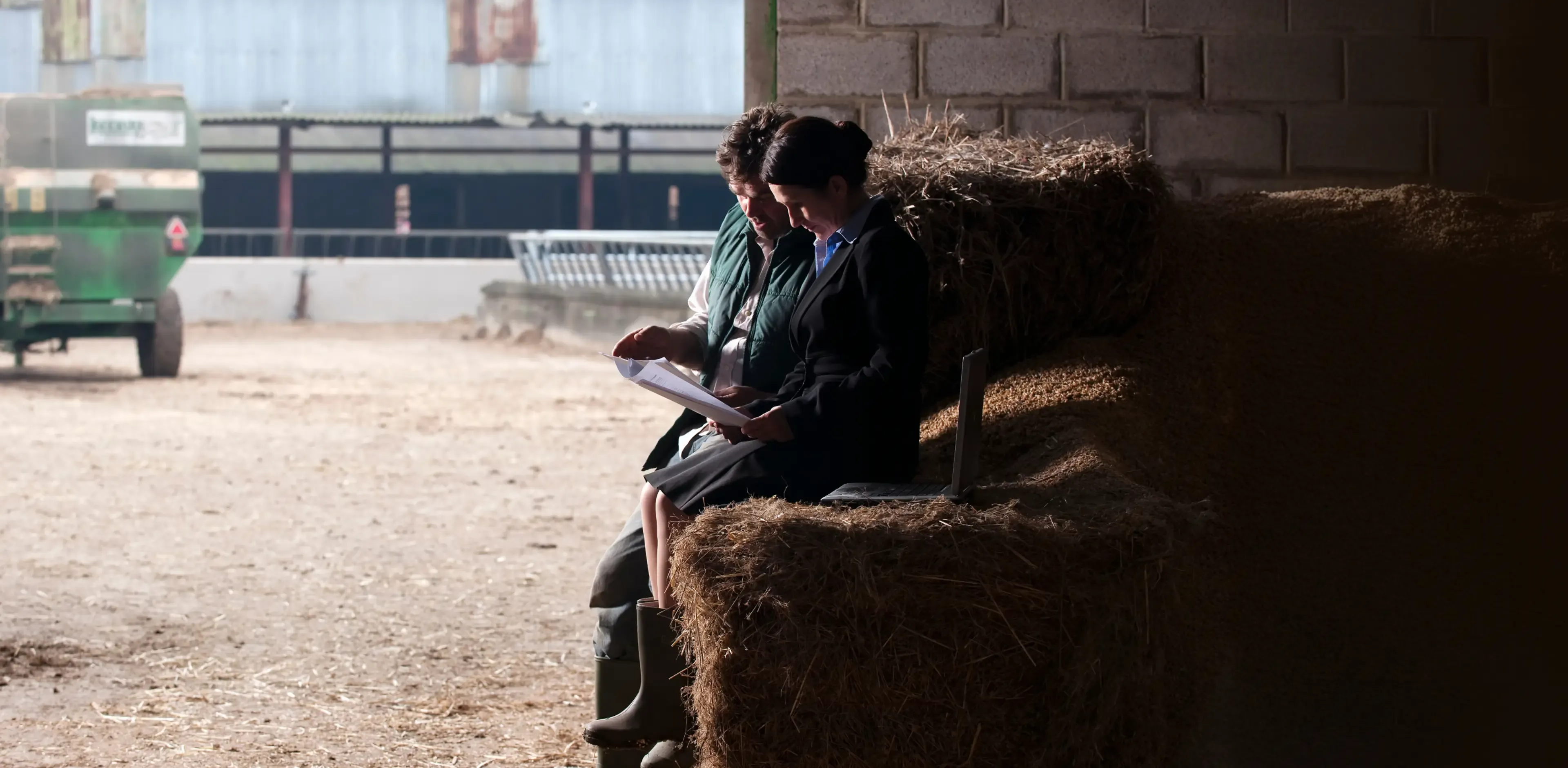 Business woman and farmer sitting on straw bales in a shed discussing business
