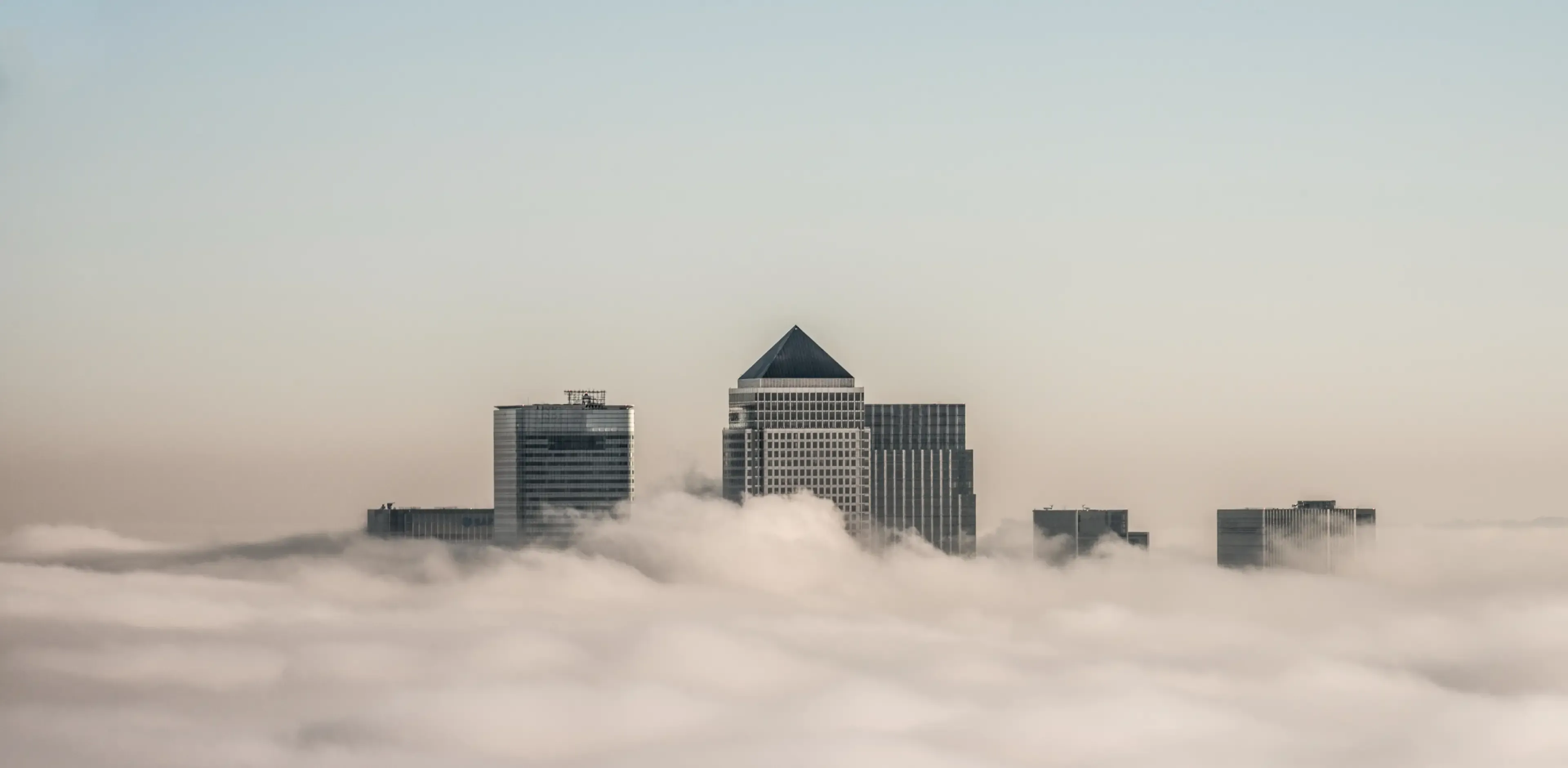 A view of the top of skyscrapers in Canary Wharf poking out above low clouds.