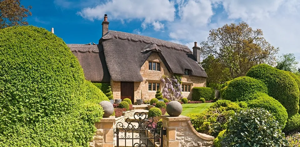 Idyllic country cottage with a thatched roof and pretty summer gardens in the Cotswolds, England