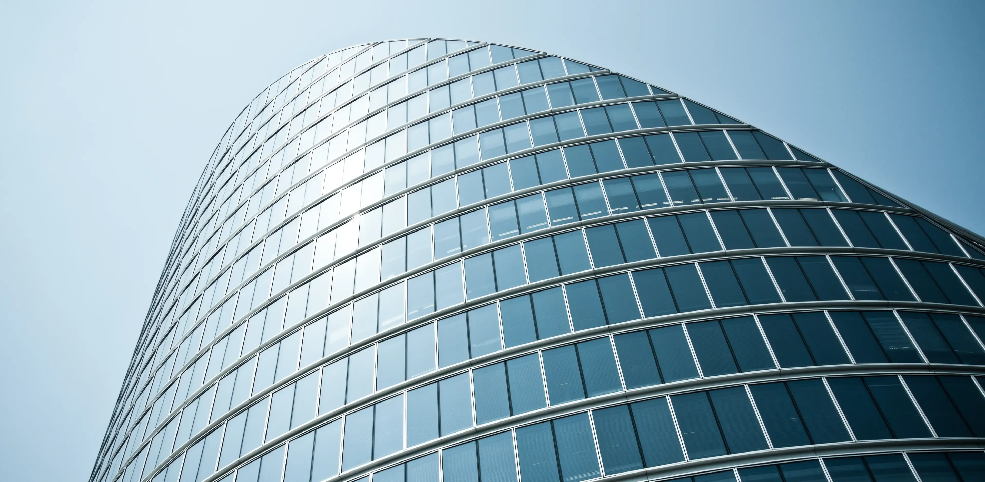 A curved, modern office building against a blue sunny sky