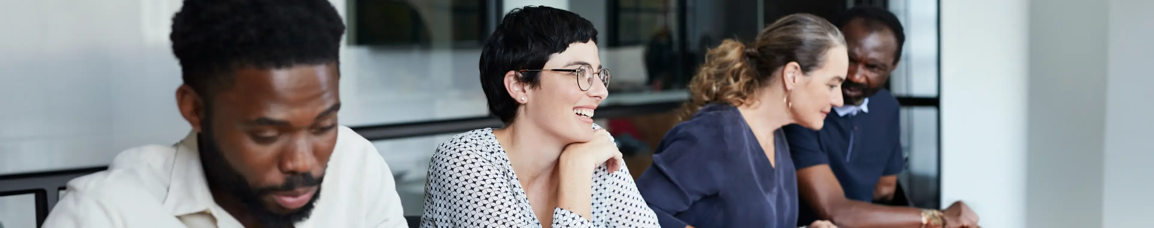 Smiling businesswoman sitting with male and female colleagues in meeting at new workplace