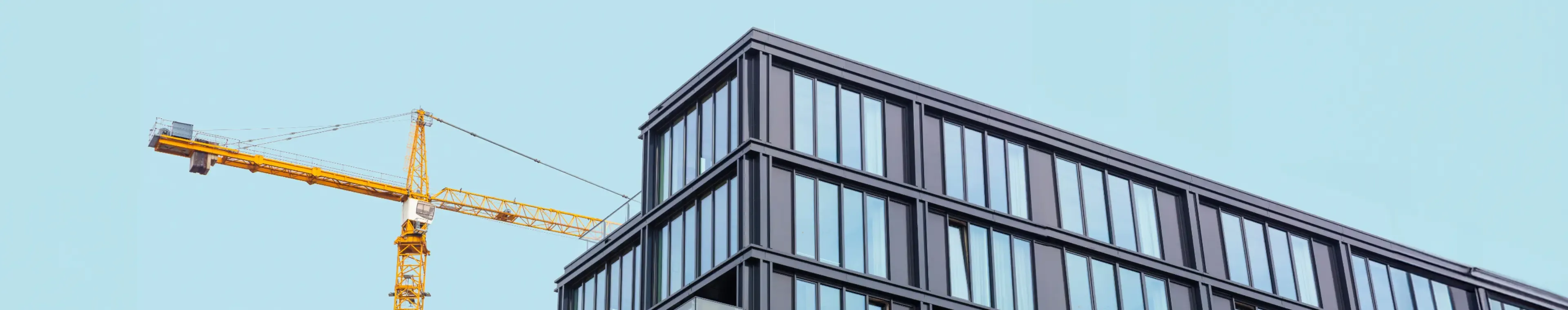 Modern apartment building under construction with a crane in the foreground against a clear blue sky.