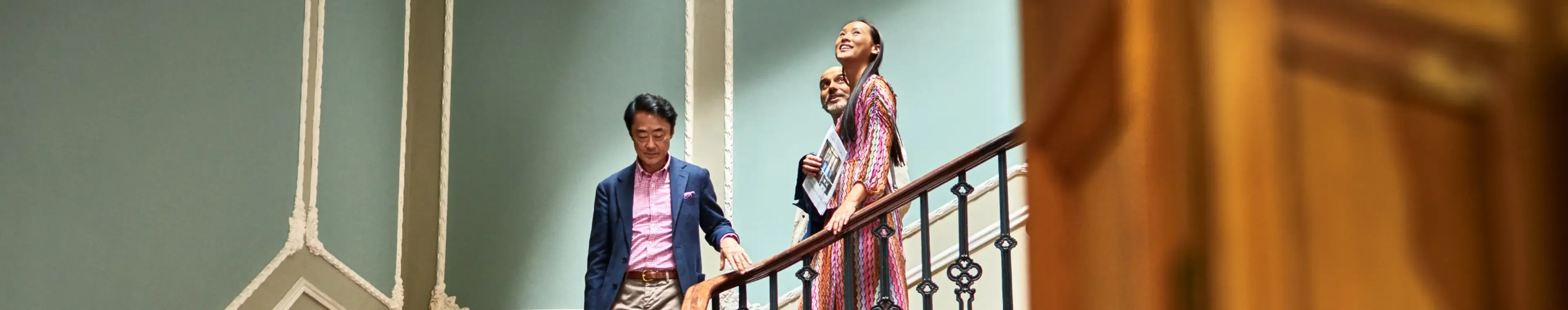 Wealthy couple walking down staircase with Japanese real estate agent during viewing in spacious potential new home, opportunity, potential, home ownership