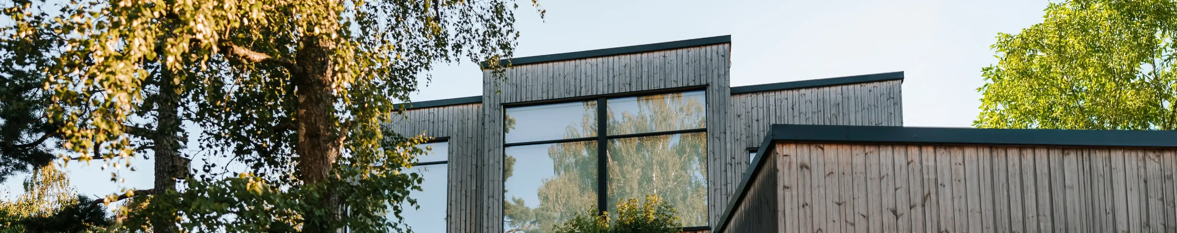 Modern wooden house with driveway and trees against sky