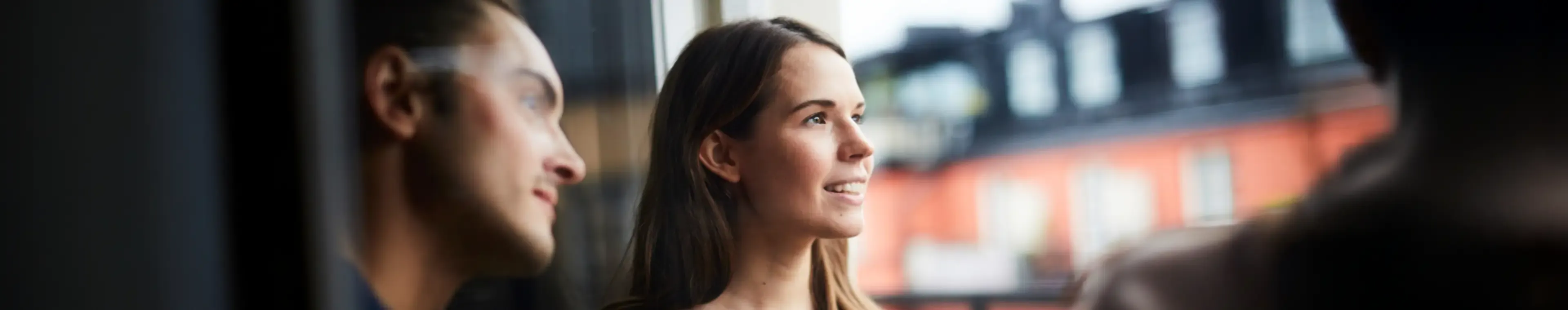 Smiling woman with friends looking away while standing in balcony of rental apartment