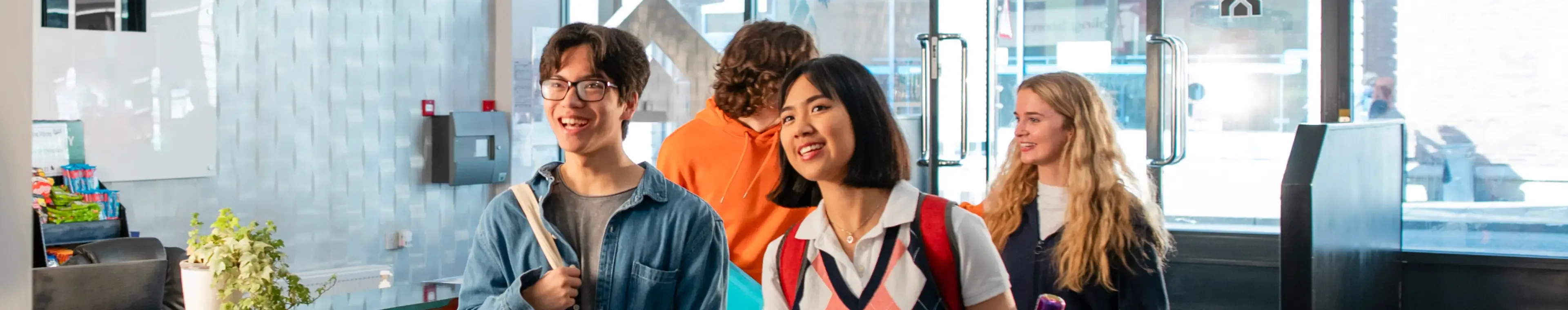Wide angle view of four new University students walking into their student accommodation in Sunderland in the north-east of England what are they was carrying a reusable toilet bag and they are walking through the reception area of the building.