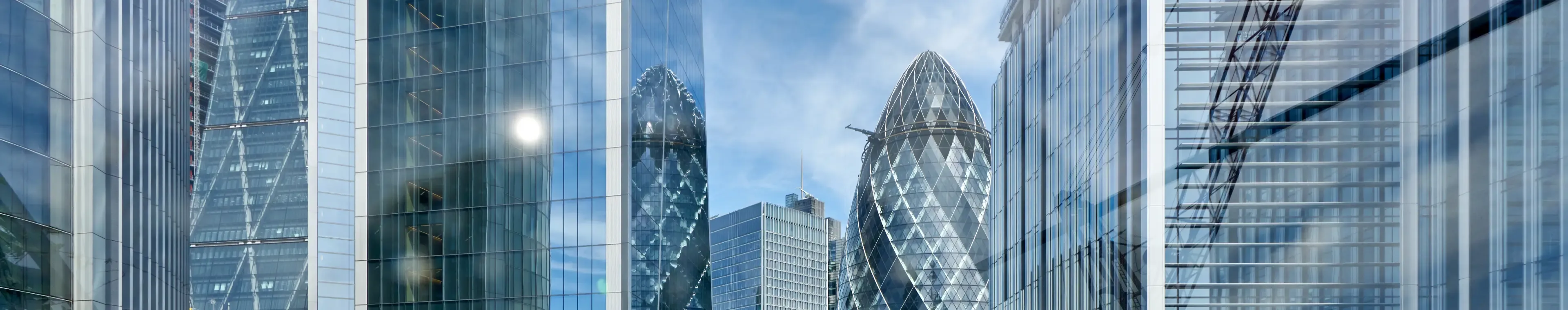 The Gherkin, formally 30 St Mary Axe and previously known as the Swiss Re Building, is a commercial skyscraper in London's primary financial district, the City of London. Here viewed looking north through glass officer buildings from the roof top of a nearby office building.