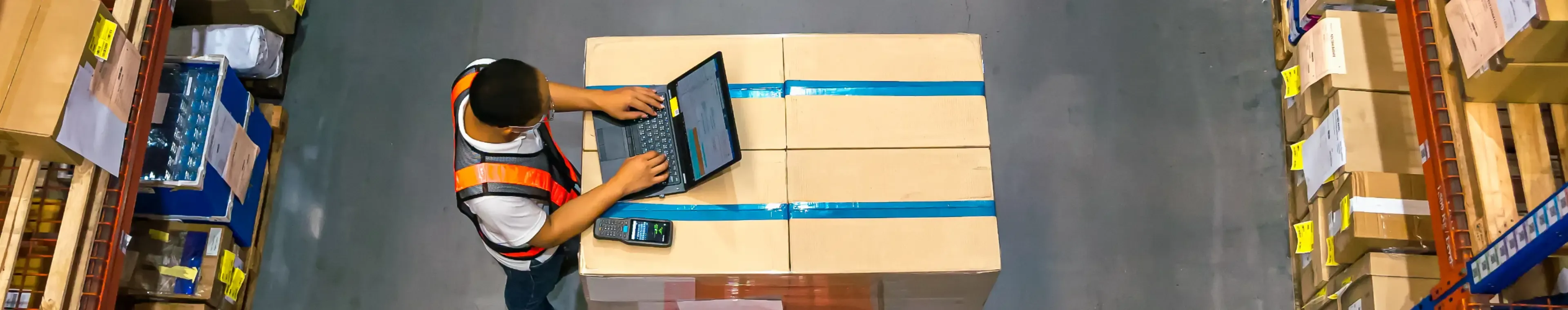 Top view of warehouse worker using laptop to check location of goods.