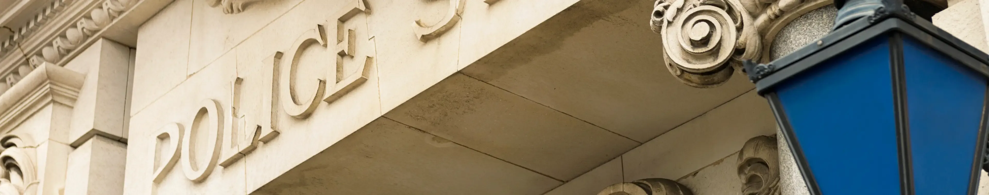 A traditional sign in the stonework above the entrance to a  police station, and a blue police lantern.