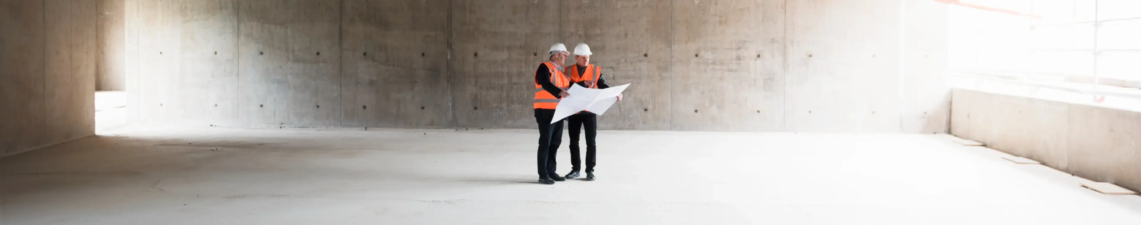 Two men with plan wearing safety vests talking in building under construction