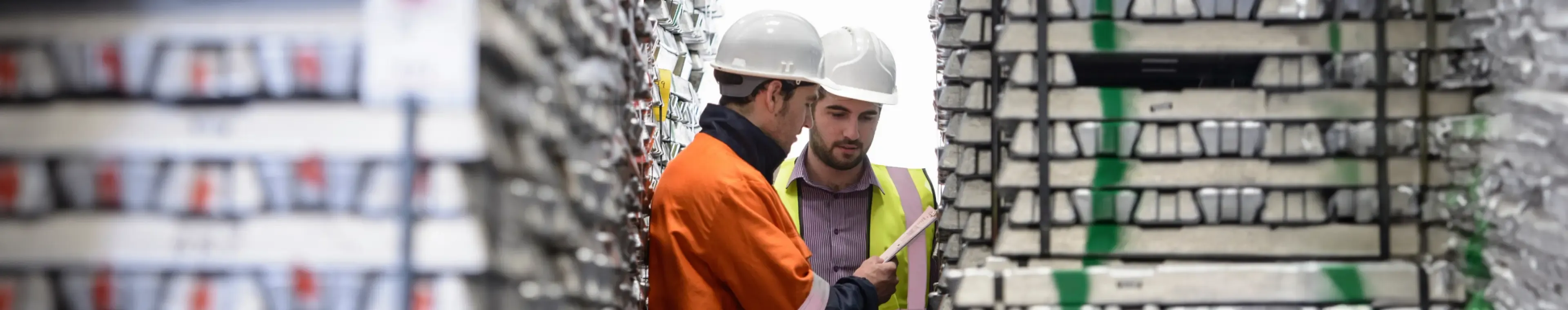 Workers inspecting stacks of aluminium ingots in warehouse